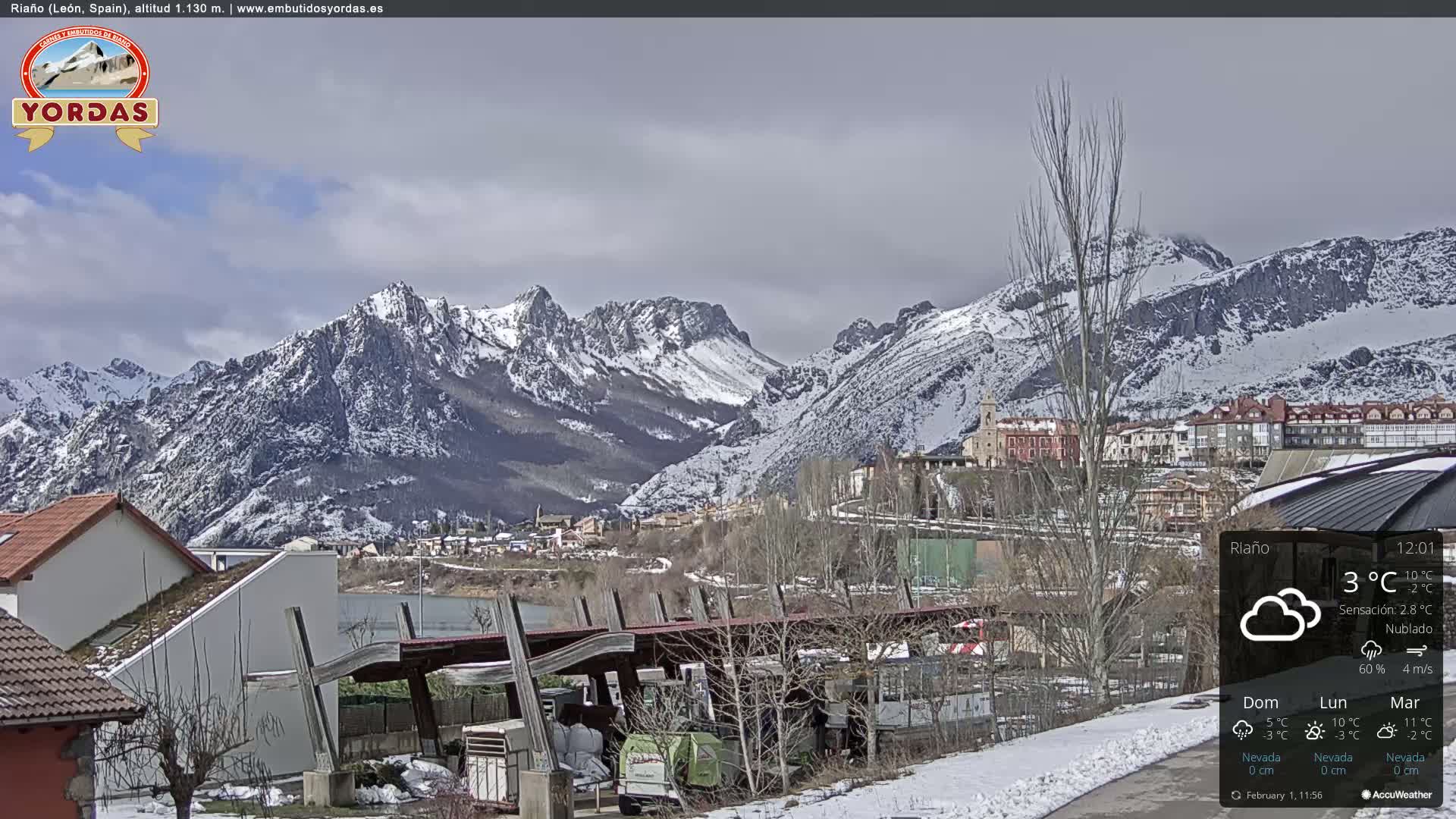 A snow-dusted town nestled in a valley, with snow-capped mountains rising in the background under a cloudy sky.