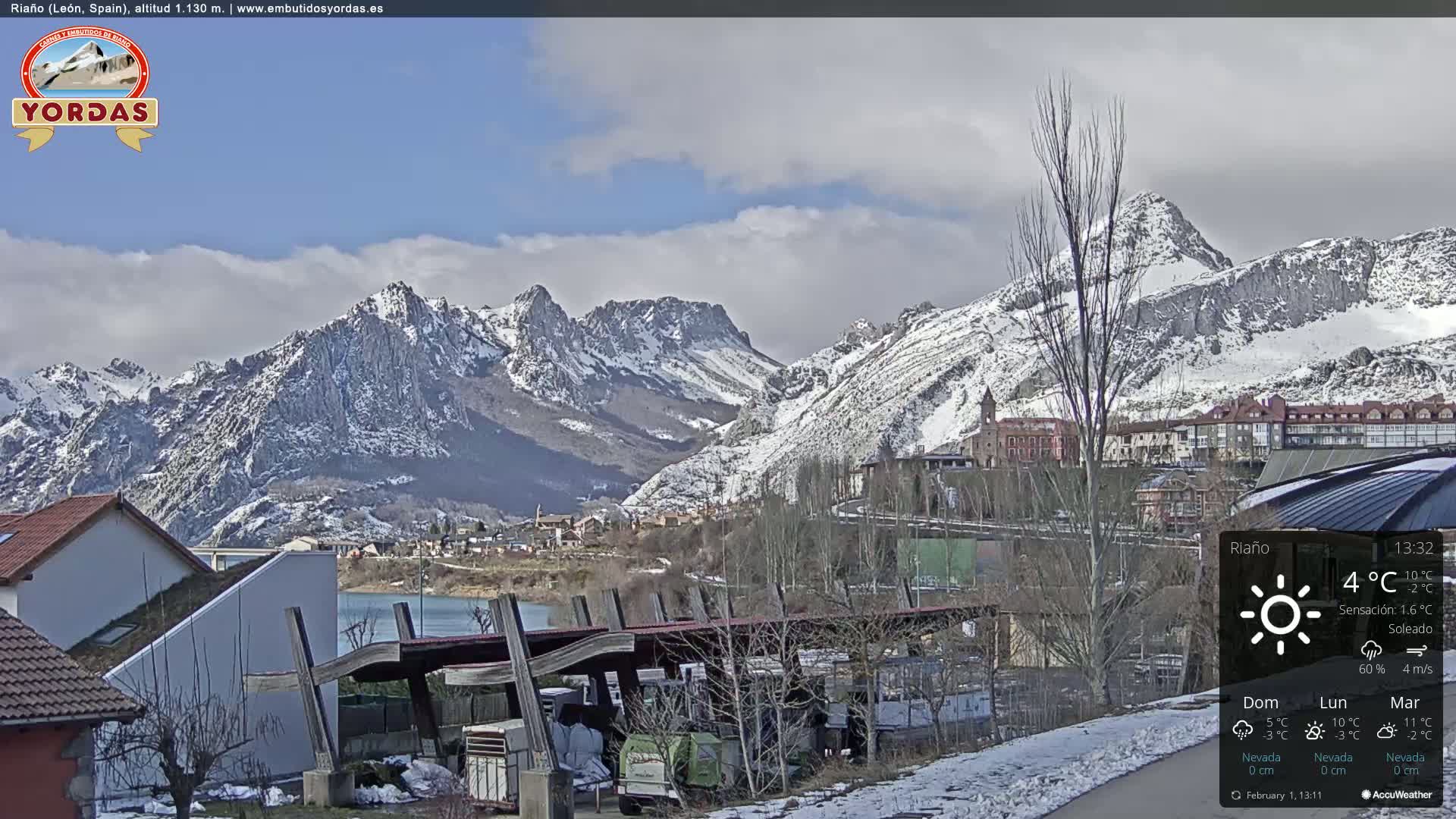 A partly cloudy day reveals a snow-dusted mountain range overlooking a town situated beside a lake.