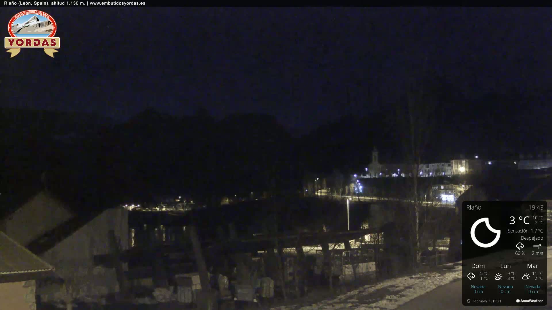 A nighttime view of a snow-dusted village nestled in a valley, under a clear, dark sky.
