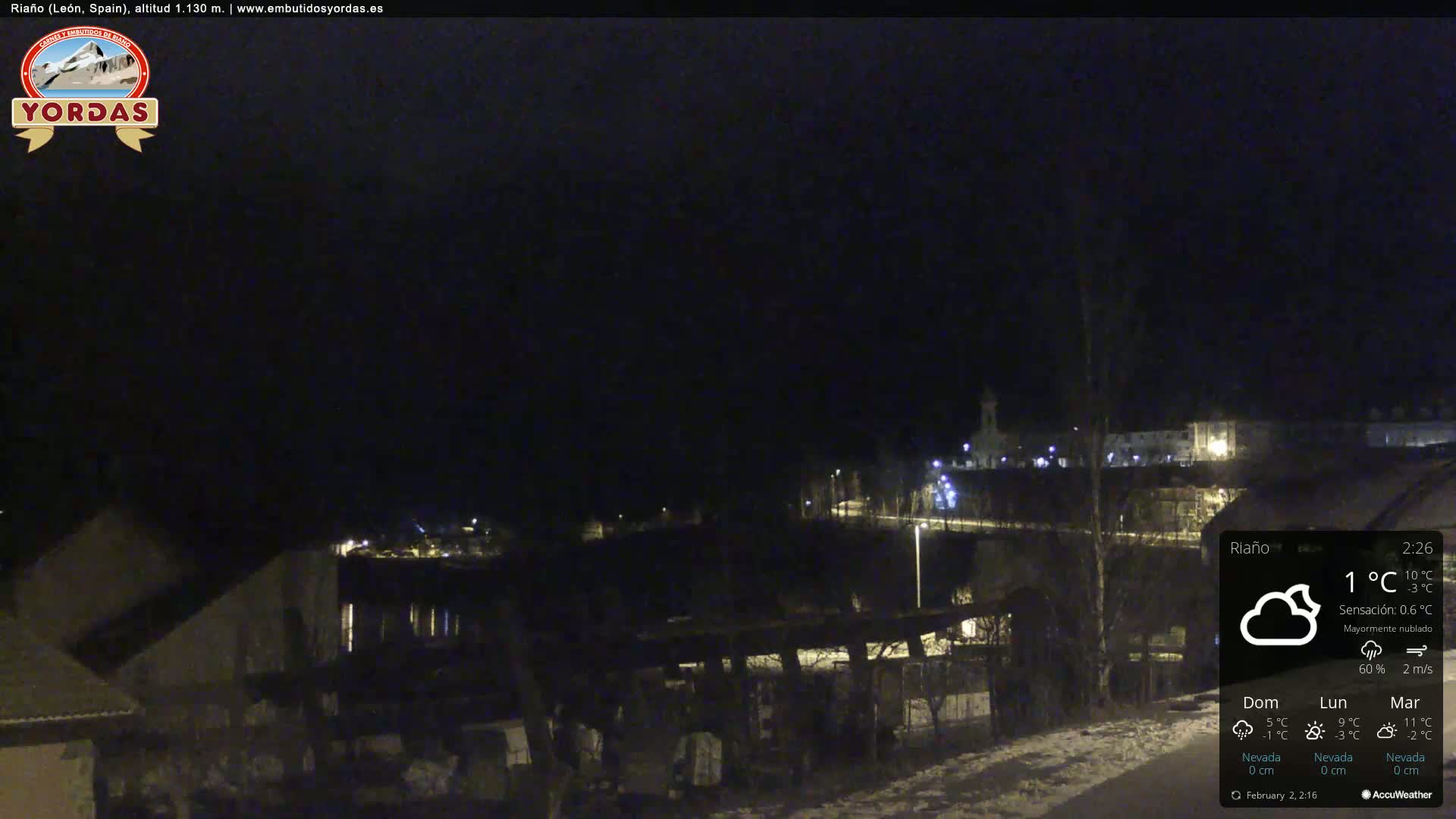 A nighttime view of a snow-dusted town under a mostly cloudy sky, with a temperature of 1°C.