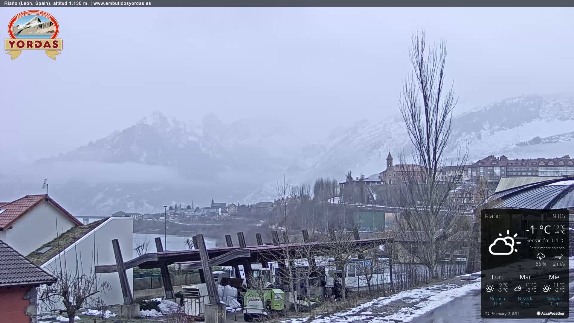 A partly sunny, cold day with a view of snow-capped mountains in the distance, overlooking a town and buildings with some snow on the ground.