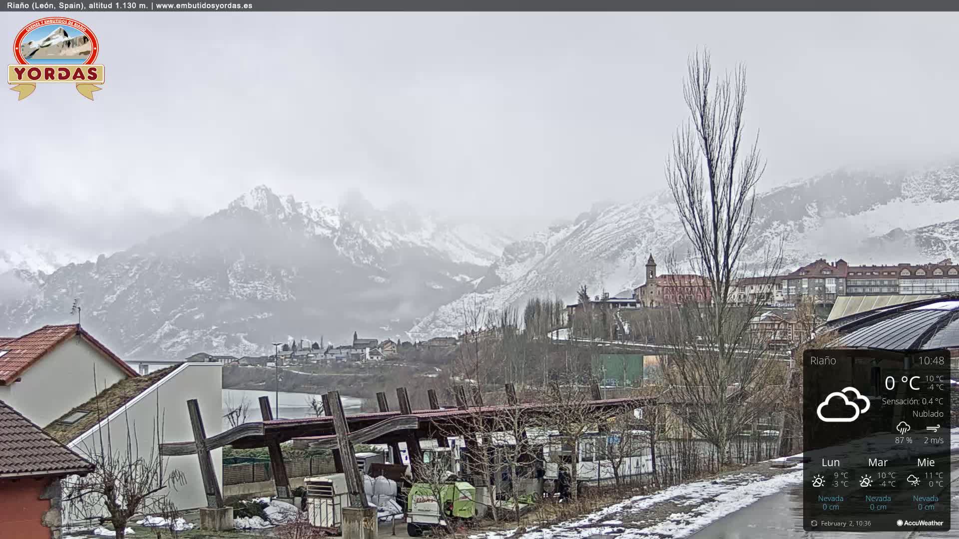 A snow-dusted town nestled in a valley between snow-capped mountains under an overcast sky.