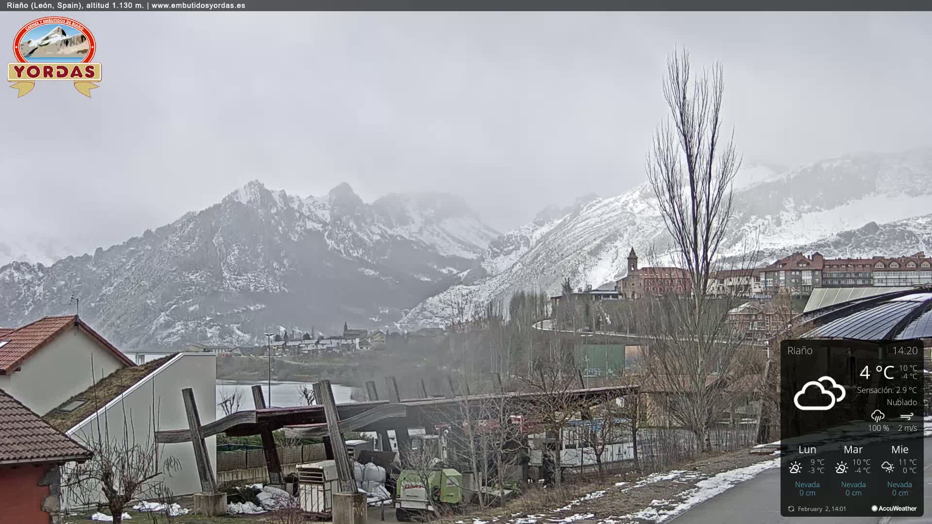 A snow-dusted mountain range looms over a town, under an overcast sky.