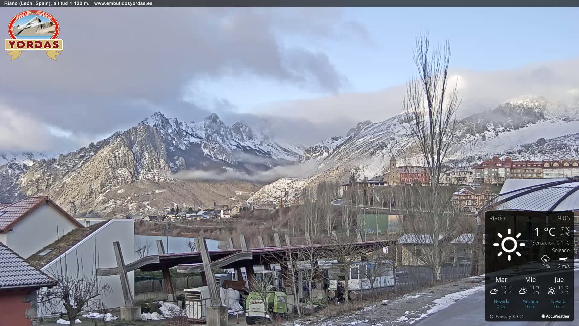 A partly cloudy day reveals a snow-dusted mountain range overlooking a small town nestled in a valley.