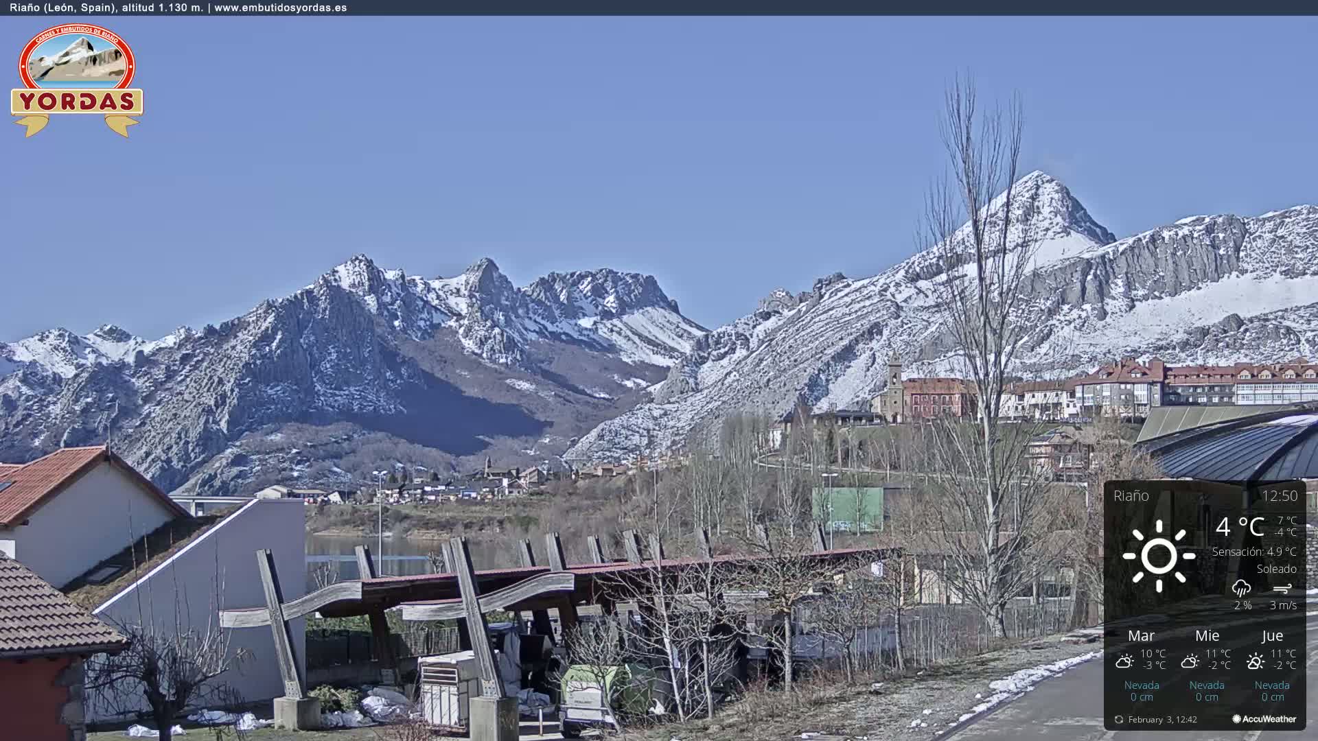 A sunny, snow-capped mountain range is visible behind a town, with a small amount of snow on the ground in the foreground.