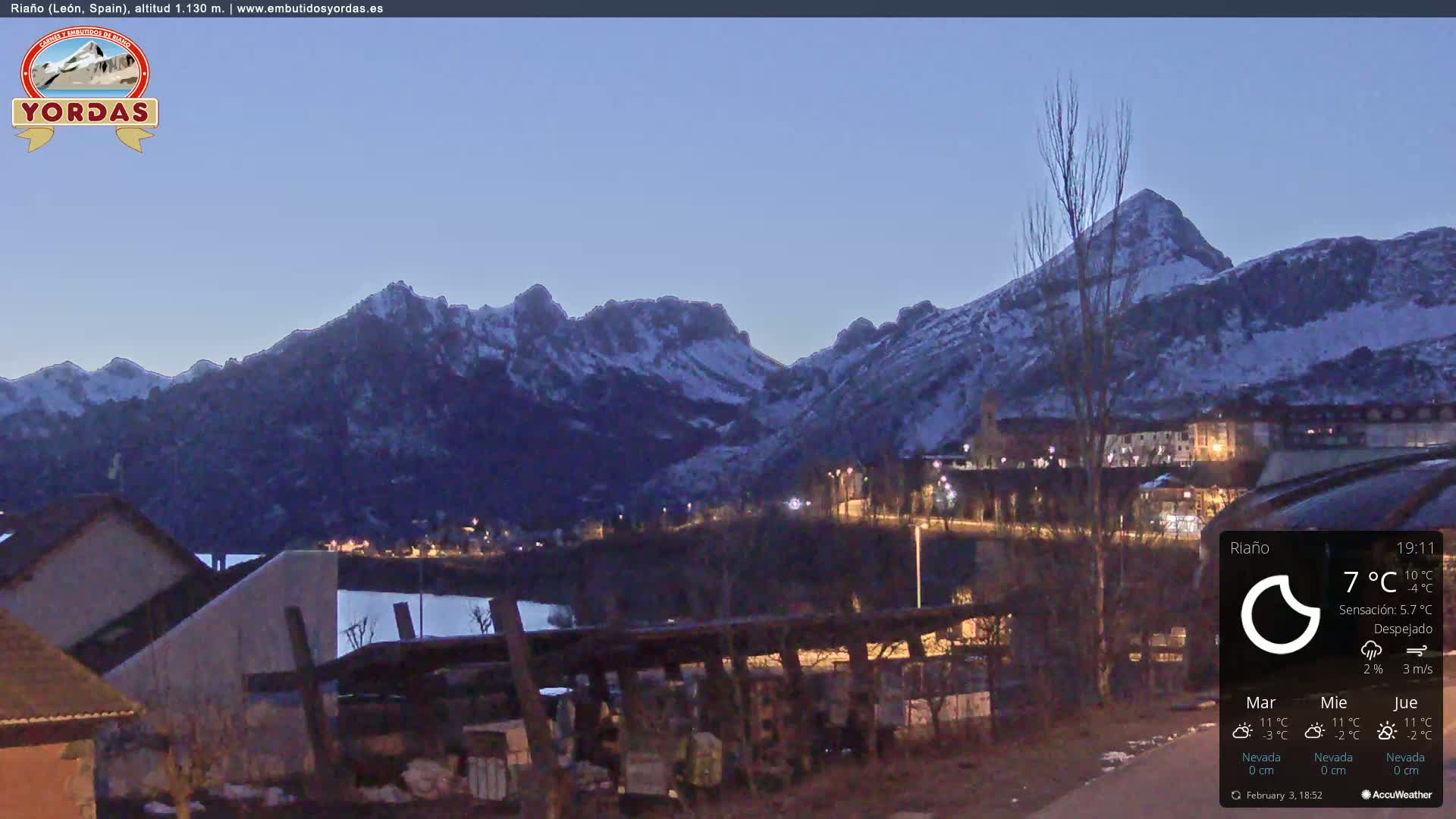 A snow-dusted mountain range is visible at twilight, overlooking a small town illuminated by lights, under a clear sky.