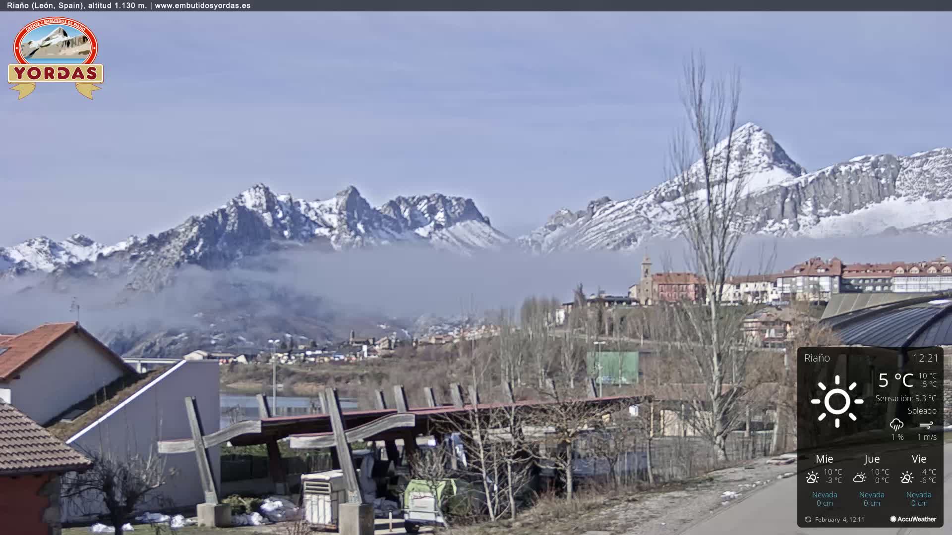 A partly cloudy day reveals a snow-capped mountain range behind a town nestled in a valley.