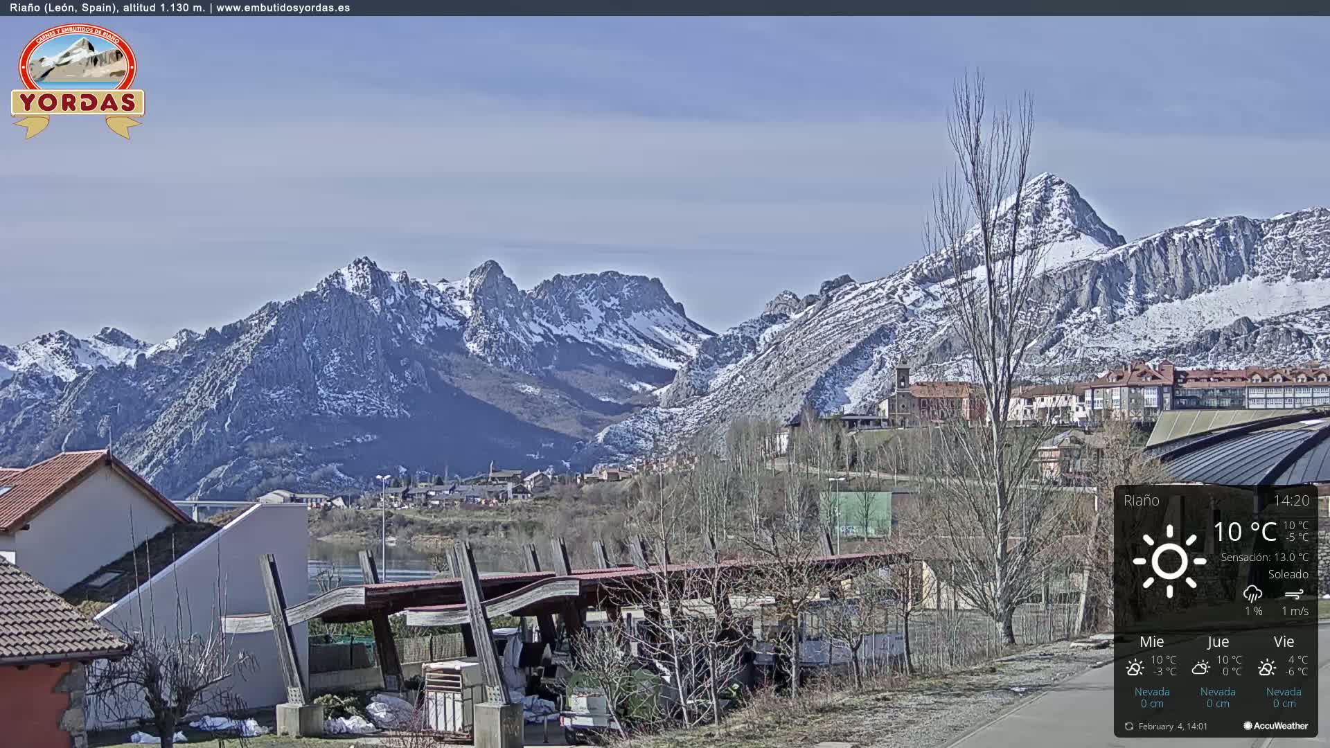 A sunny view of a snow-capped mountain range overlooking a town with buildings and a covered structure.
