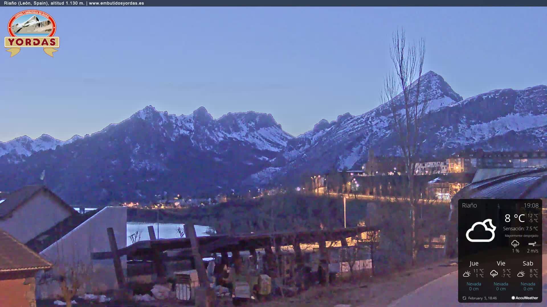 A twilight view of snow-capped mountains overlooking a town, under a mostly clear sky.