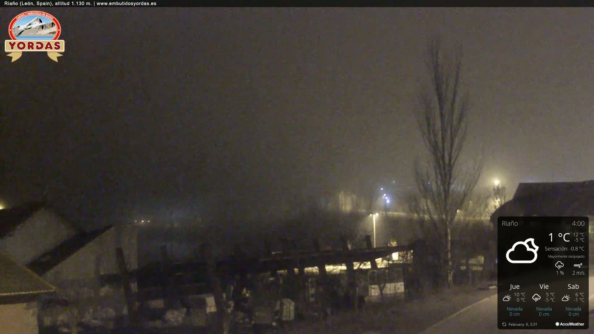 A nighttime view of a sparsely populated area shrouded in fog, with a few lights visible in the distance.