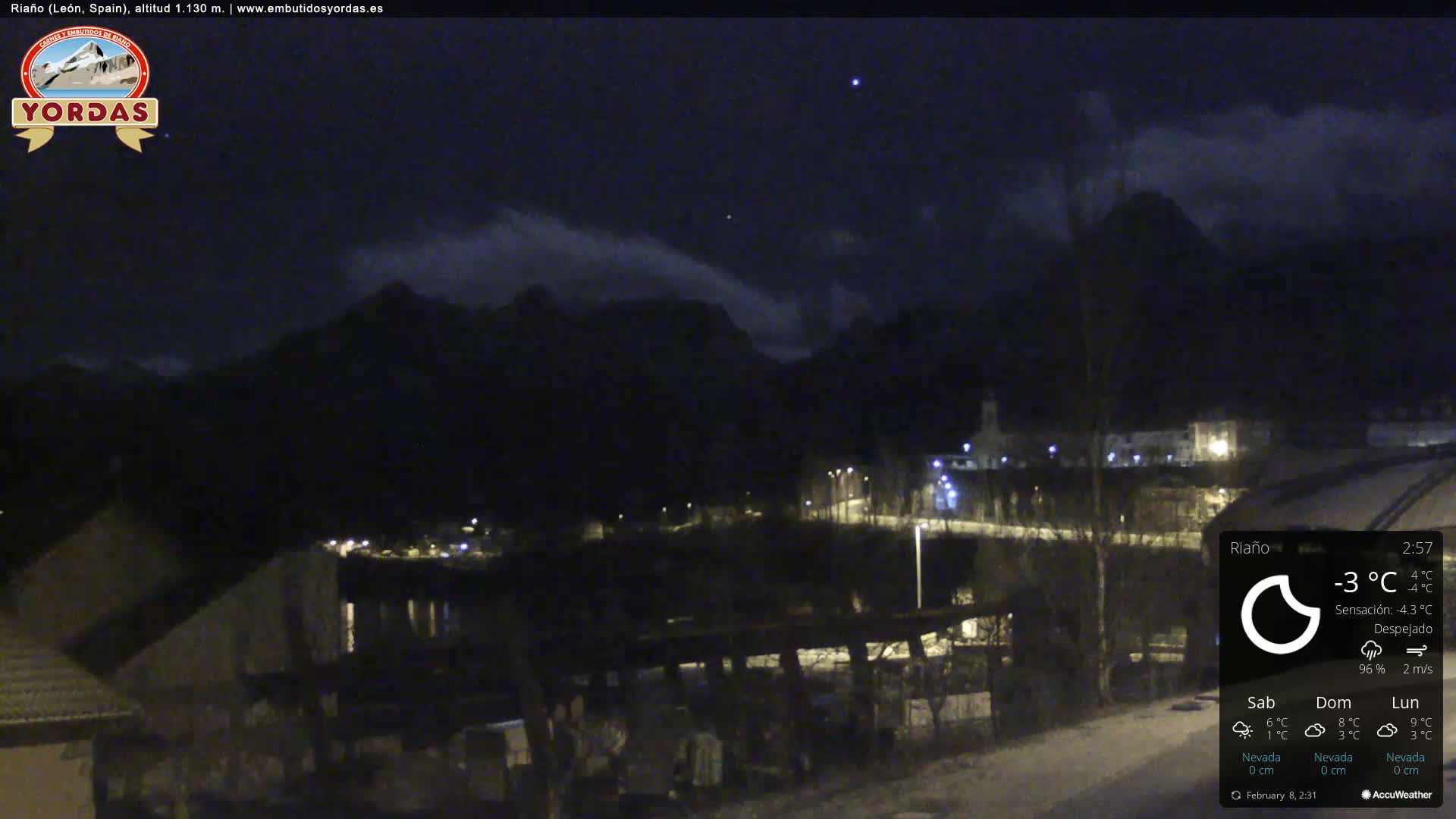 A nighttime view of a snow-covered town nestled beneath dark mountains under a mostly clear sky.