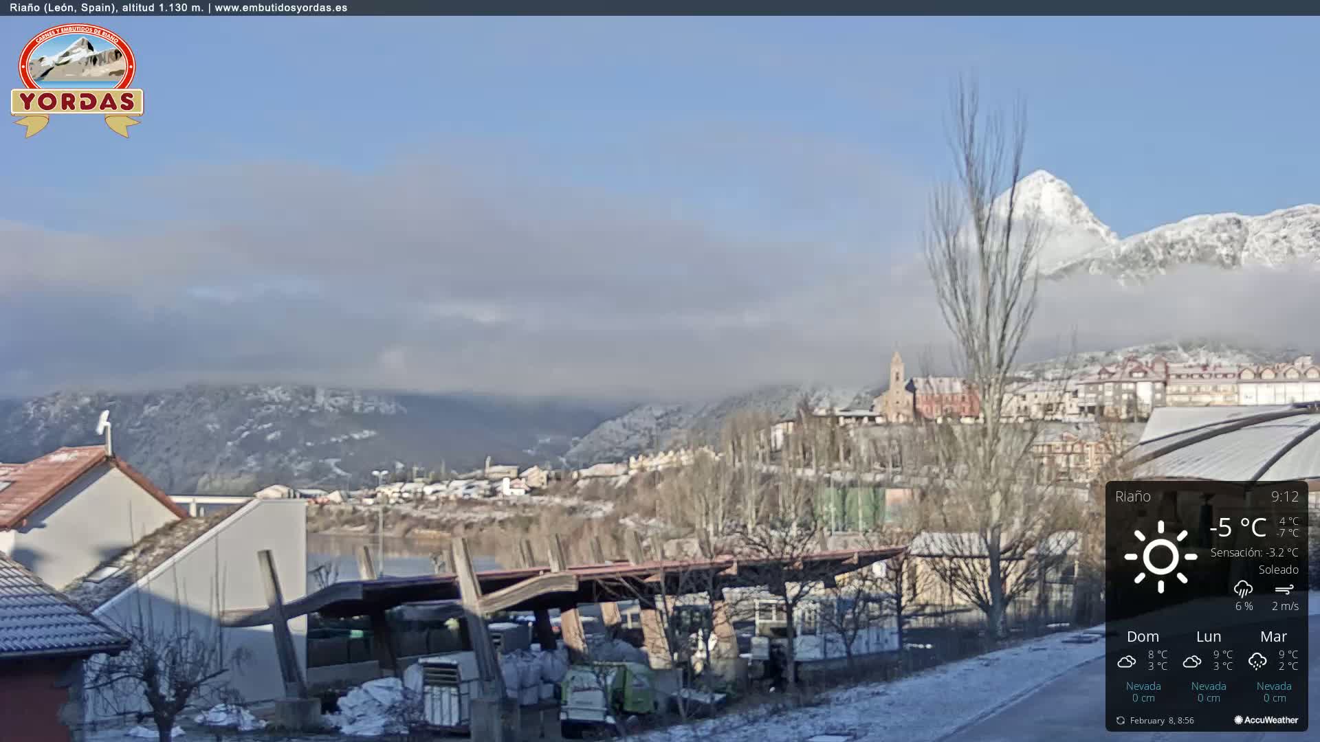 A partly sunny, cold day in a snow-dusted town nestled in a valley, with mountains capped with snow in the background.