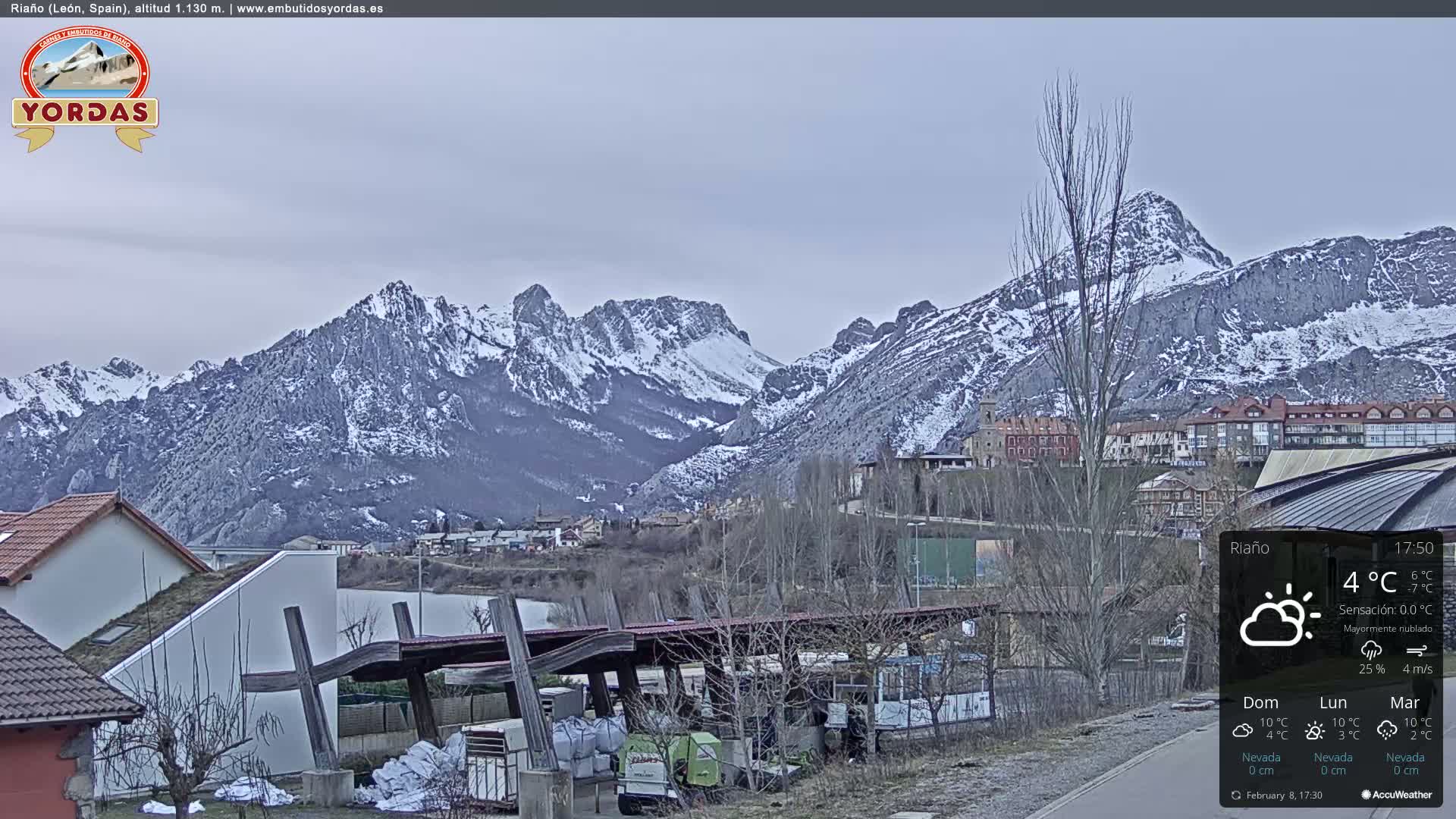 A partly cloudy, cool day overlooking a snow-dusted mountain range and a small town nestled at its base.