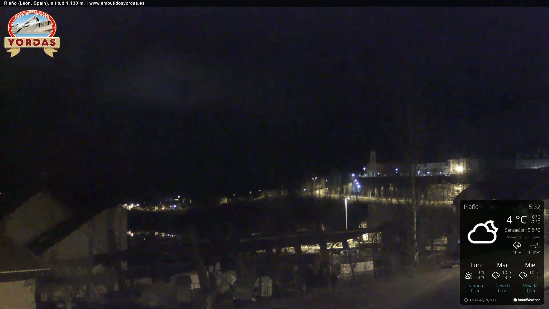A nighttime view of a small town with its lights illuminated under a mostly cloudy sky.