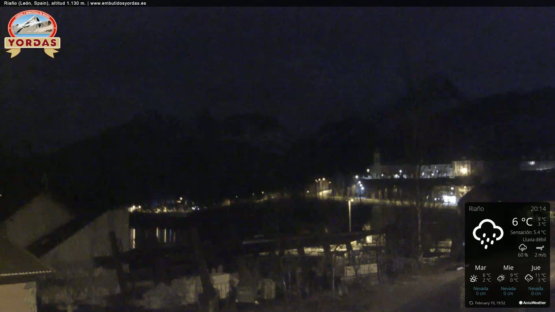 A nighttime view of a town nestled in a valley, under a dark sky with light rain.