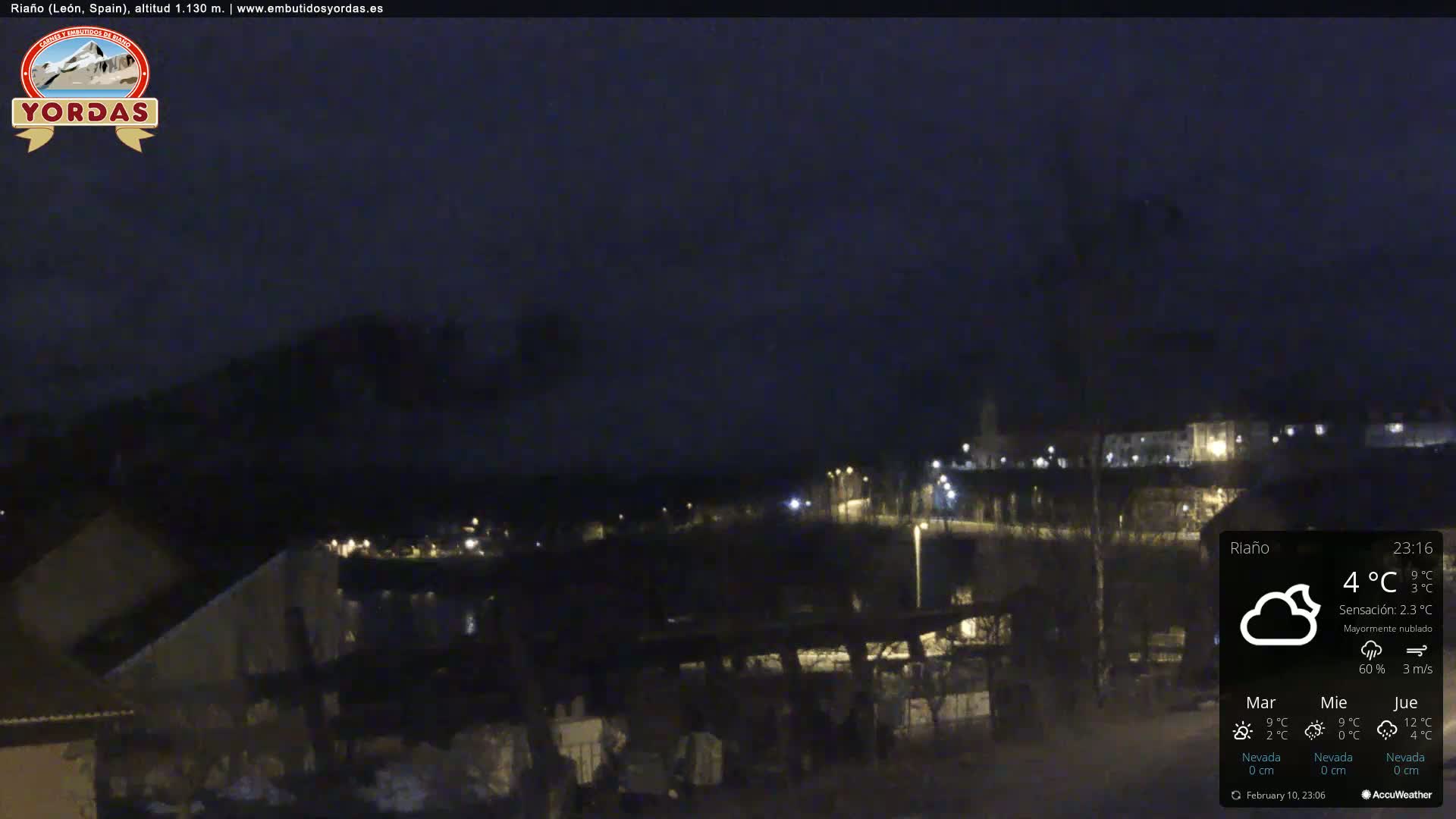 A nighttime view of a town illuminated by streetlights under a mostly cloudy sky.