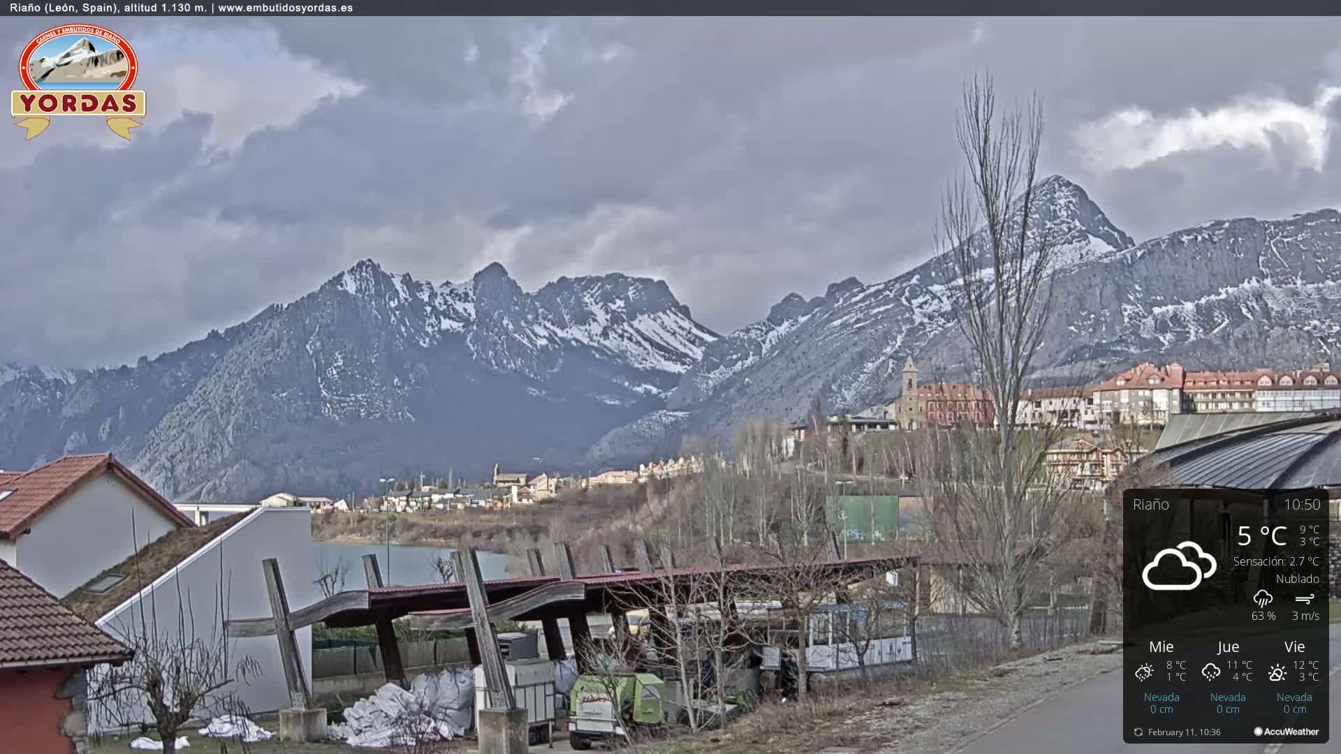 A partly cloudy day reveals a town nestled at the foot of snow-capped mountains.