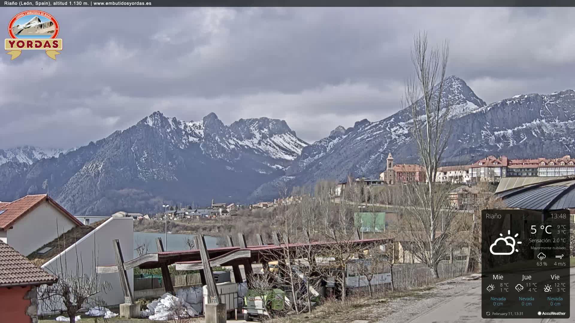 A mostly cloudy view of a town nestled in a valley, with snow-capped mountains in the background.