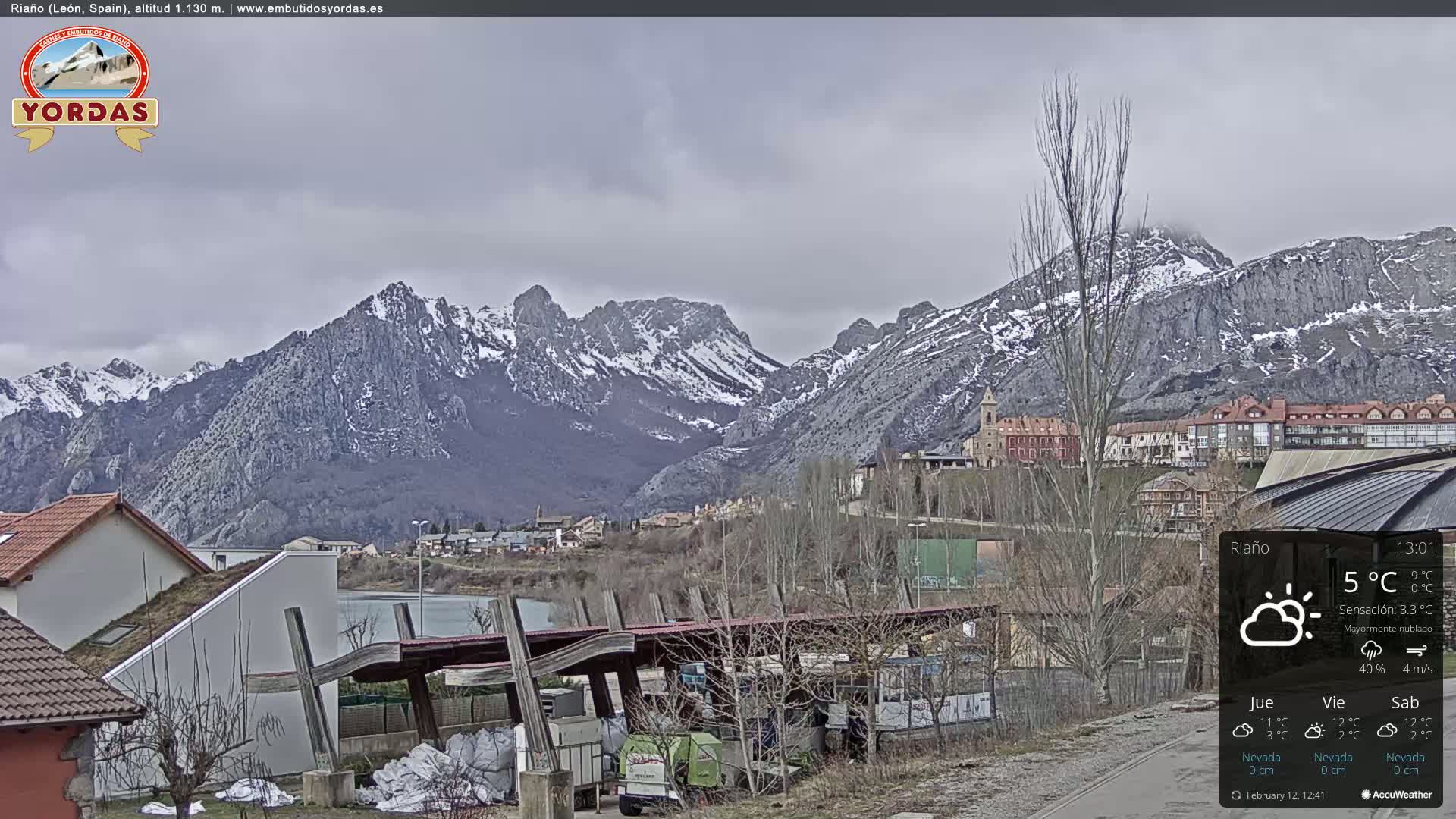 A town nestled in a valley, overlooked by snow-capped mountains under a mostly cloudy sky.
