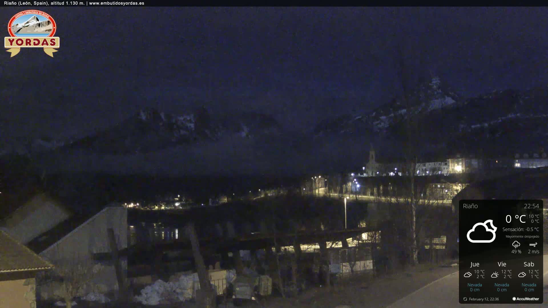 A nighttime view of a town nestled in a valley, with mountains in the background under a mostly clear sky.