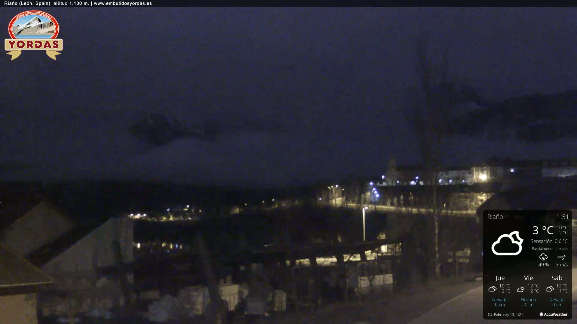 A nighttime view of a town nestled in a valley, partially obscured by clouds under a dark sky.