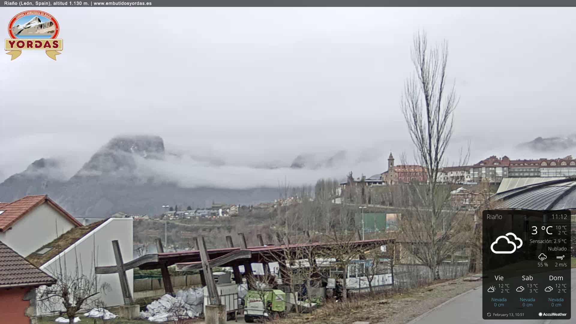 A foggy town nestled in a valley between mountains, with a cloudy sky.