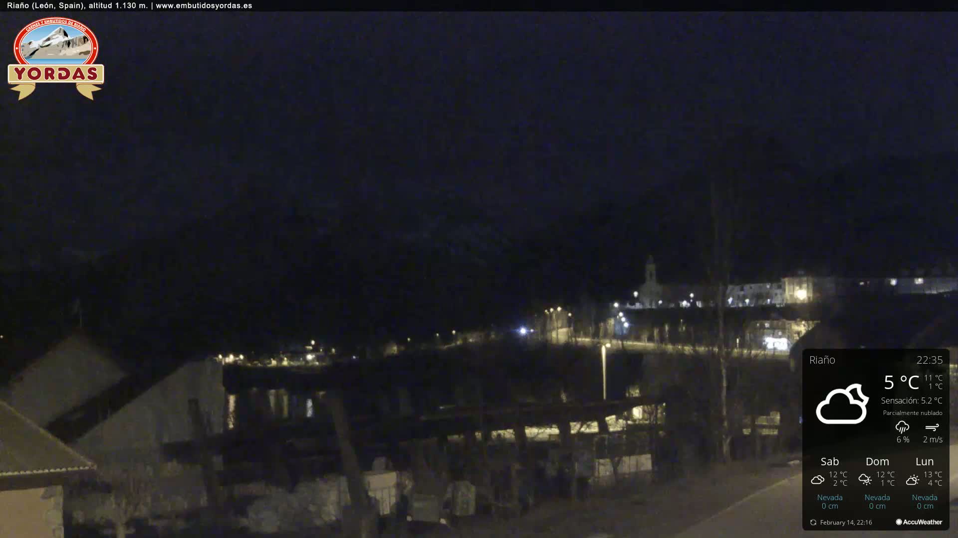 A nighttime view of a small town nestled in a valley, partially obscured by clouds under a dark sky.