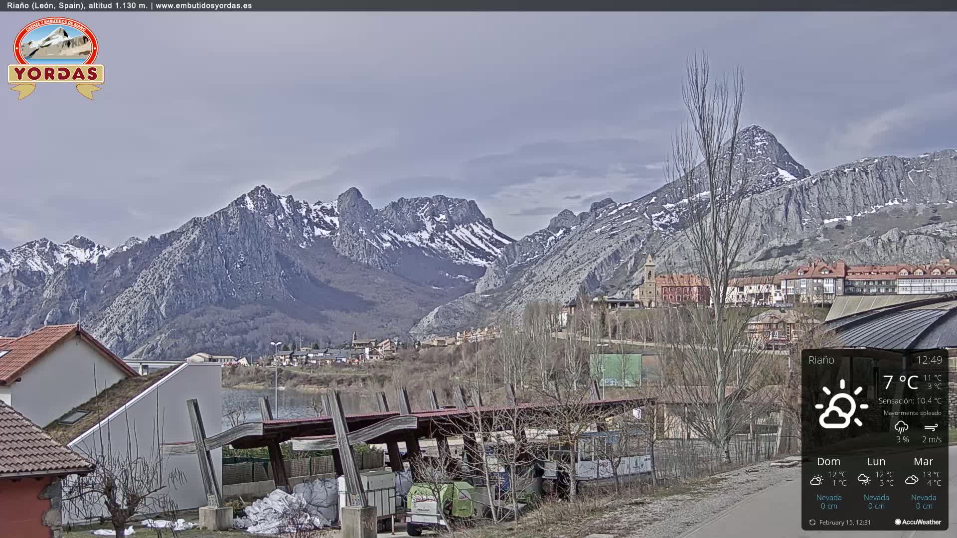 A town nestled in a valley, overlooked by snow-capped mountains under a mostly sunny sky.