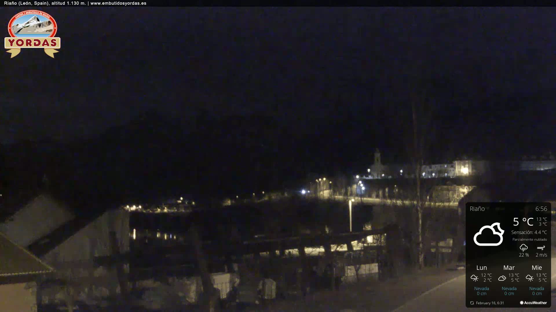 A nighttime view of a small town nestled in a valley, under a partly cloudy sky.