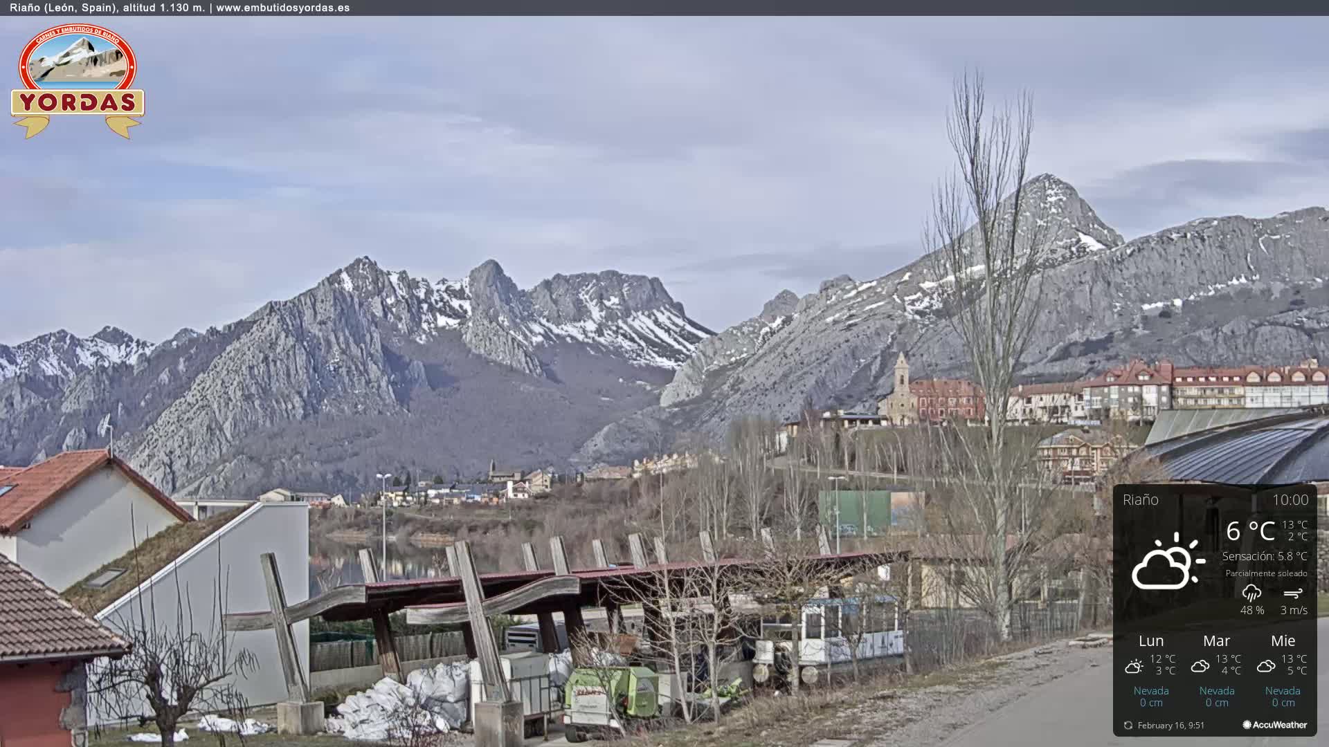 A partly sunny view of a town nestled at the foot of snow-capped mountains.