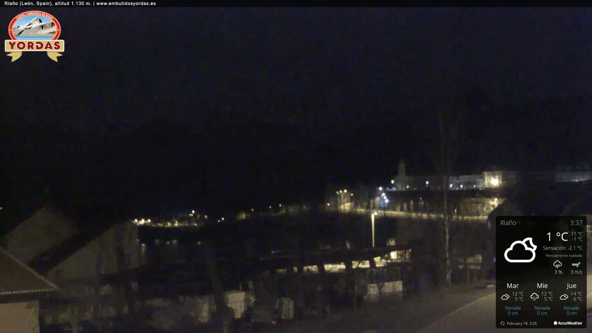 A nighttime view of a small town, partially obscured by darkness, under partly cloudy skies.