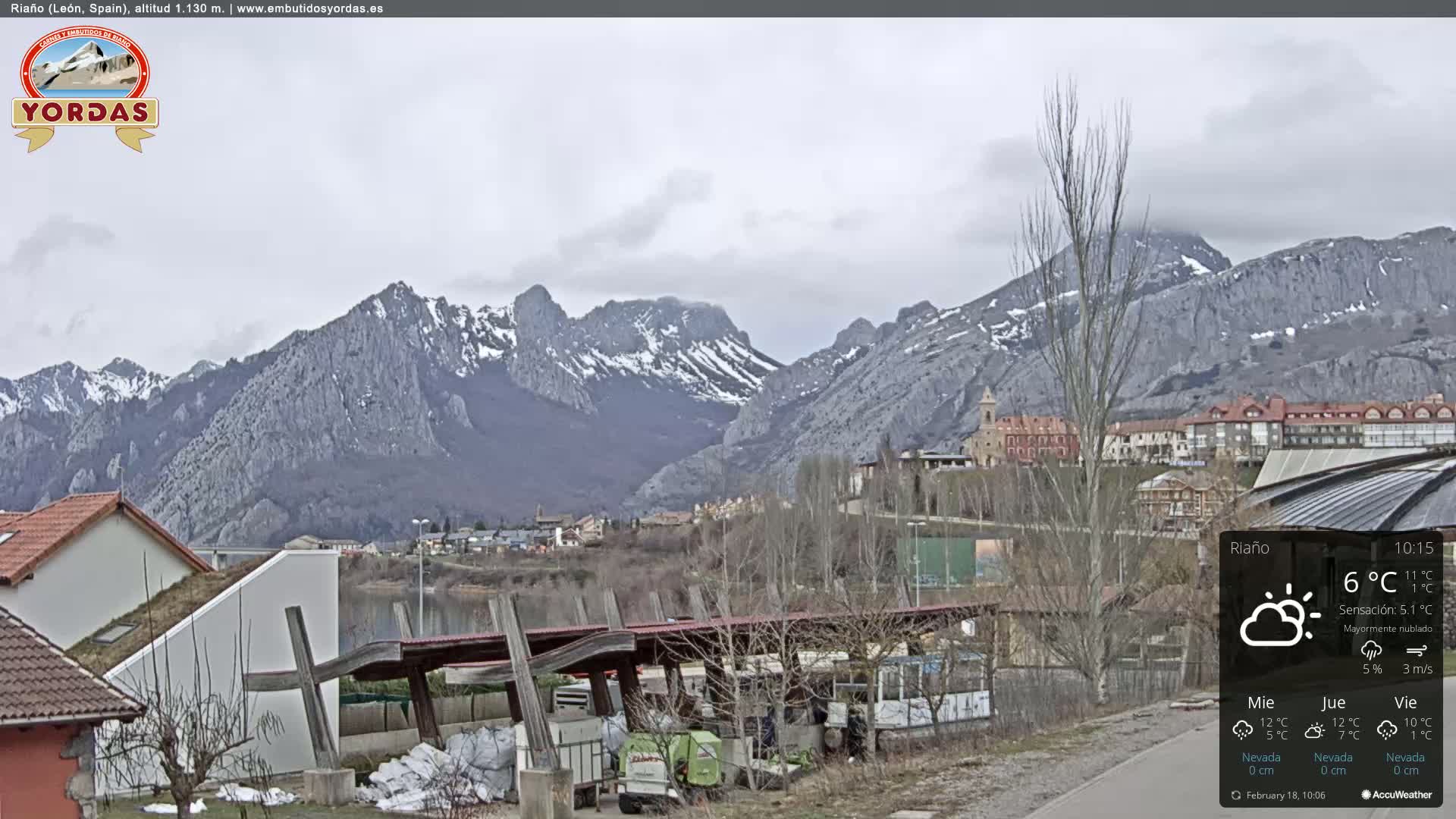 A mostly cloudy view of a snow-dusted mountain range behind a town nestled beside a lake.