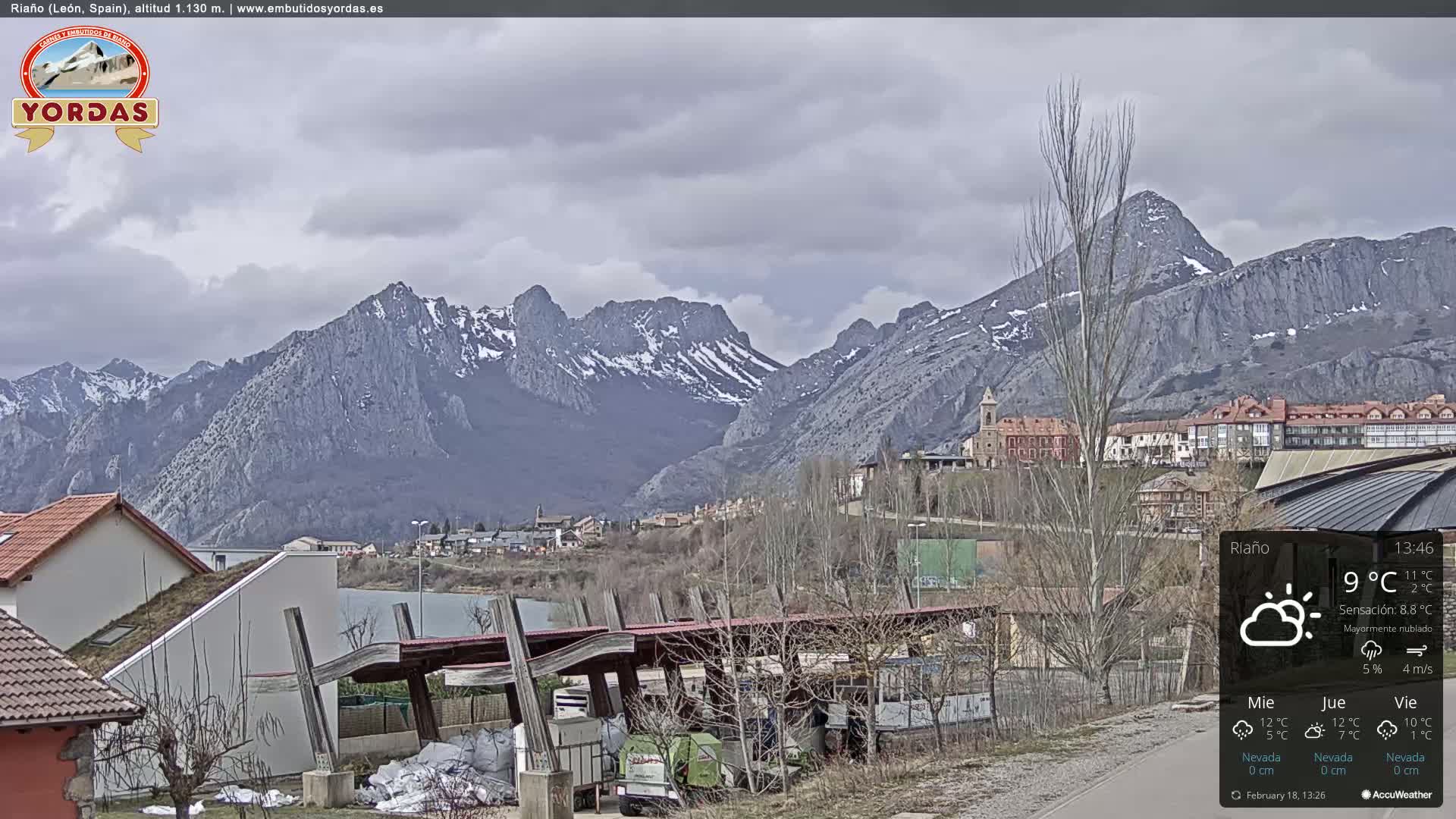 A town nestled in a valley is overlooked by snow-capped mountains under a mostly cloudy sky.