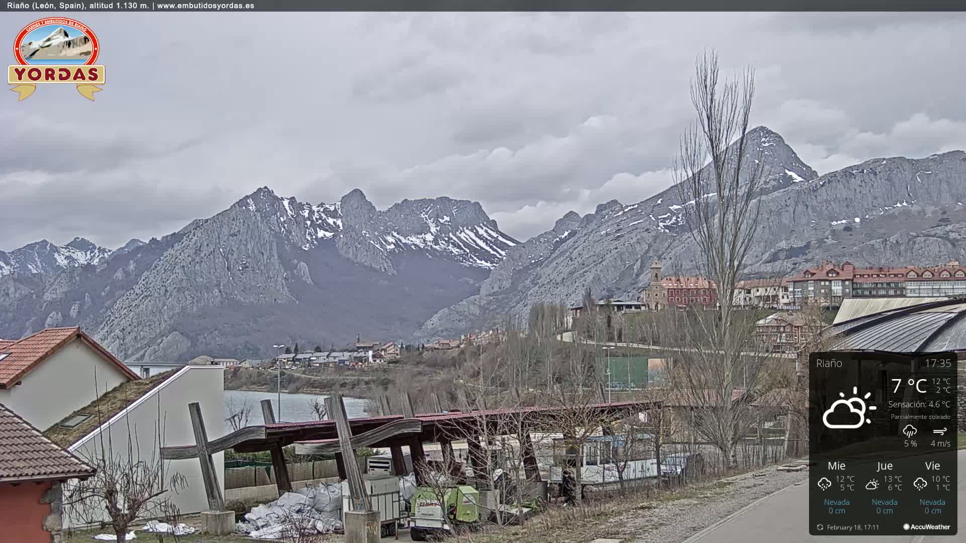 A partially sunny view of a town nestled in a valley, backed by snow-dusted mountains.