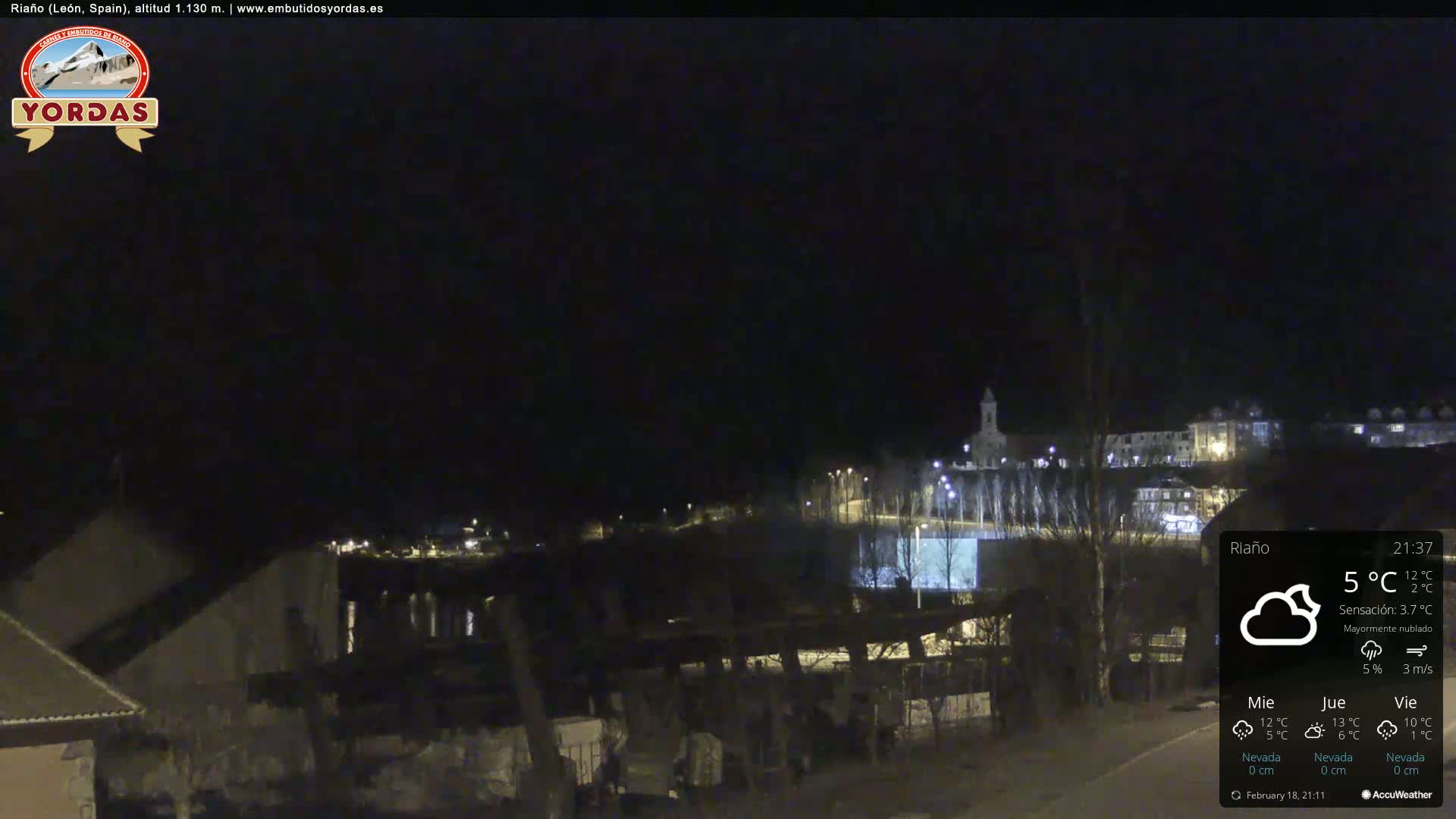 A nighttime view of a town, mostly dark with some lights visible, under a mostly cloudy sky.