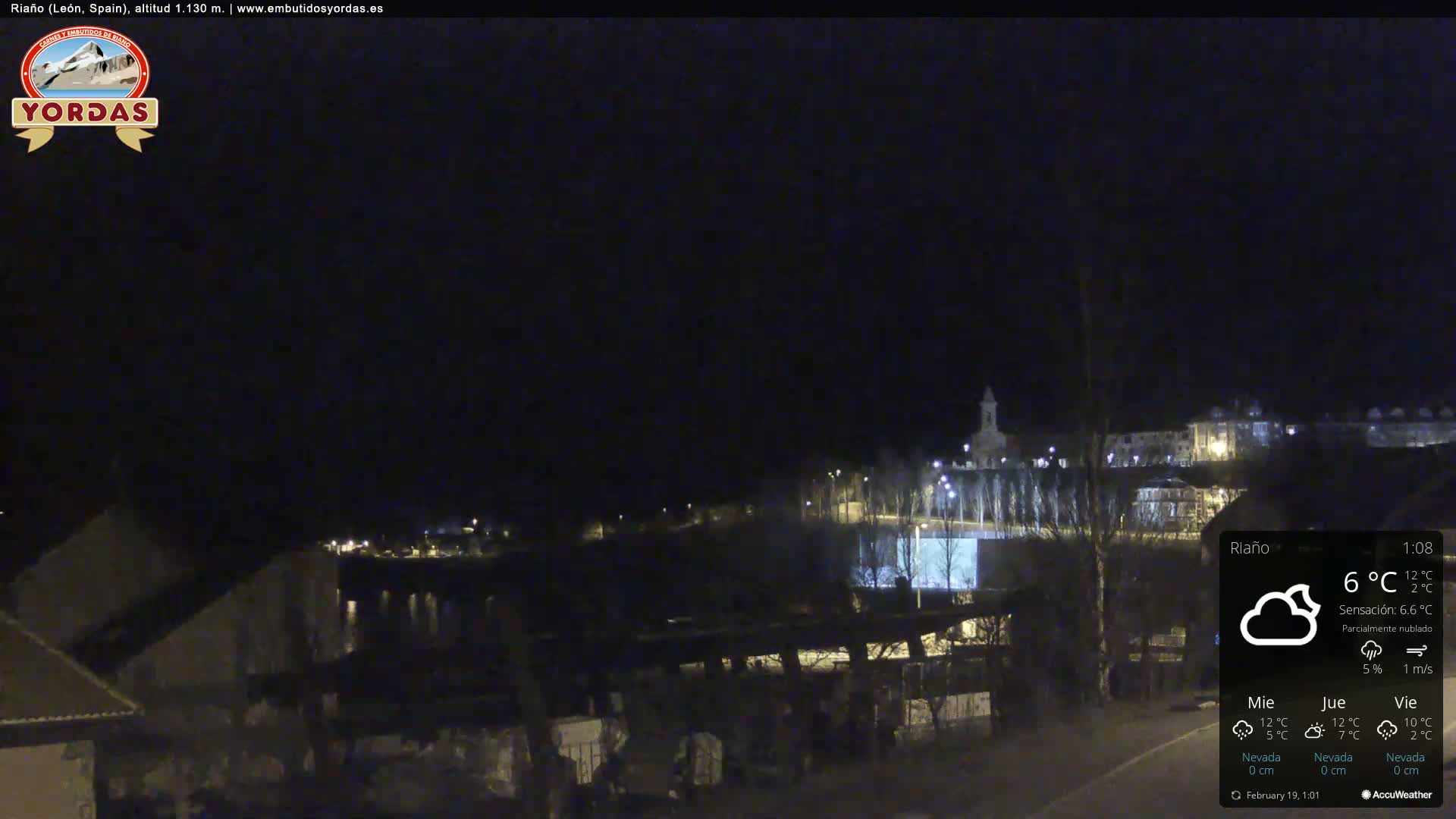 A nighttime view of a town, partially obscured by darkness, under partly cloudy skies.