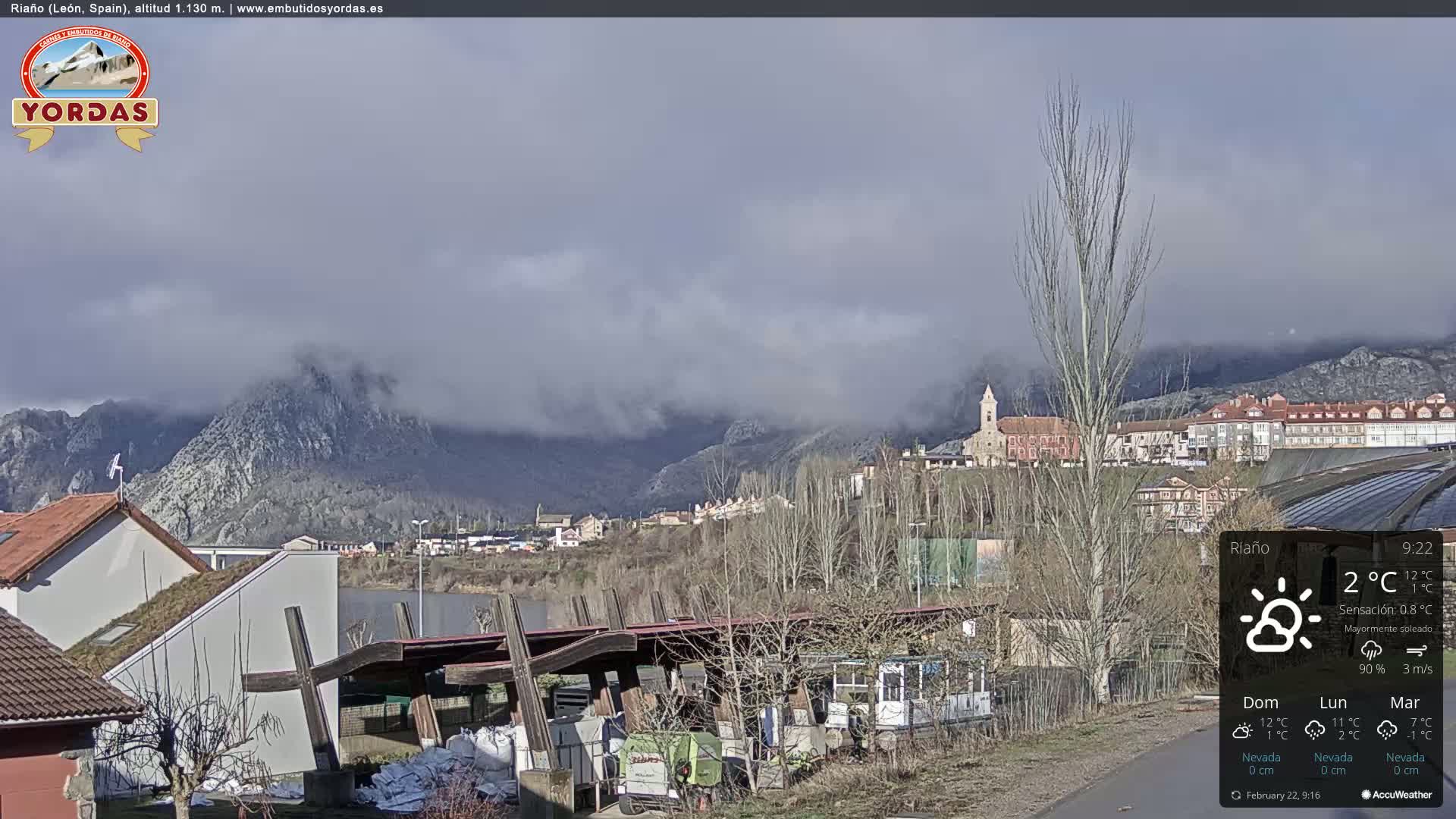 A partly cloudy day reveals a town nestled beside a lake and mountains partially shrouded in fog.