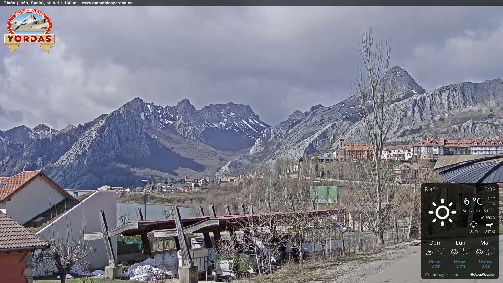 A partly cloudy day reveals a town nestled at the base of snow-capped mountains.