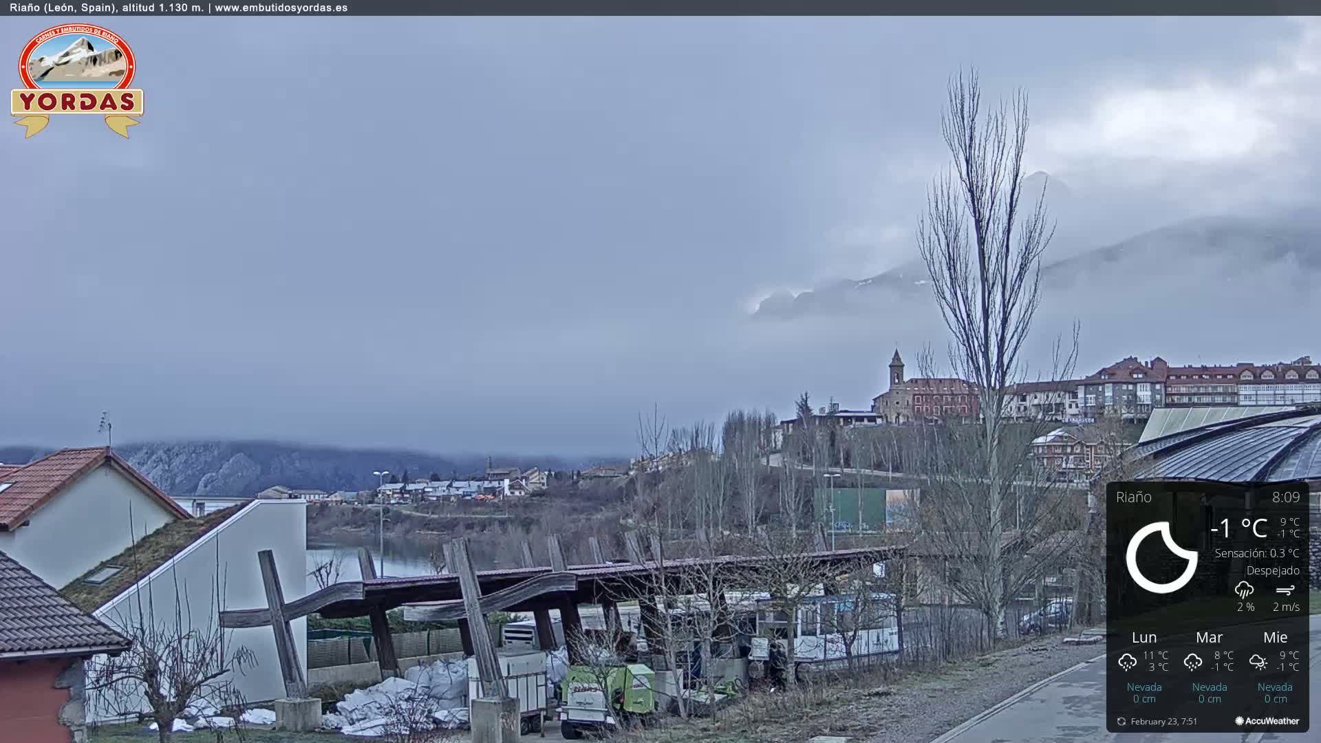 A foggy, overcast view of a town nestled beside a body of water, with mountains shrouded in mist in the background.