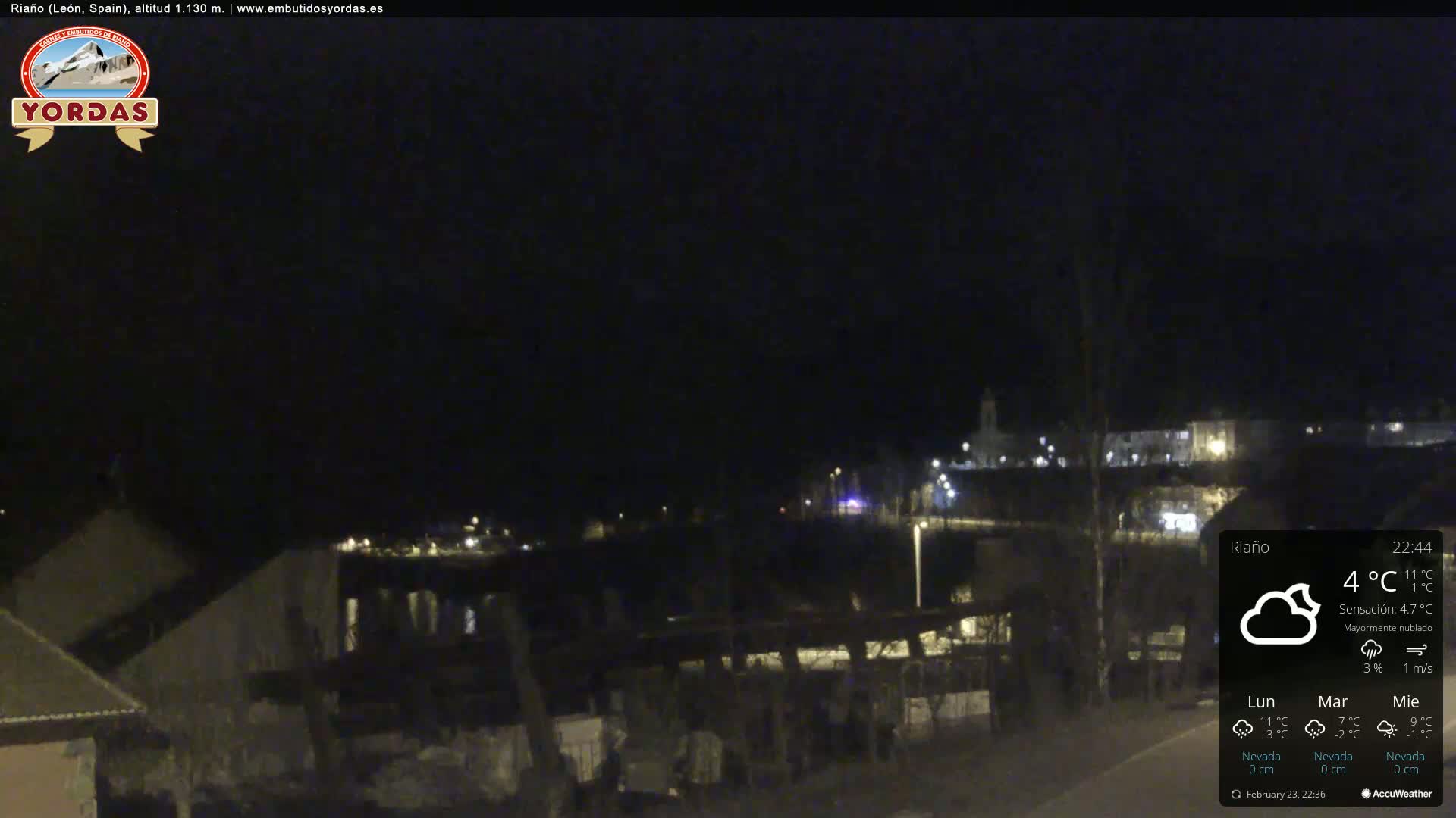 A nighttime view of a town, mostly obscured by darkness, under mostly cloudy skies.