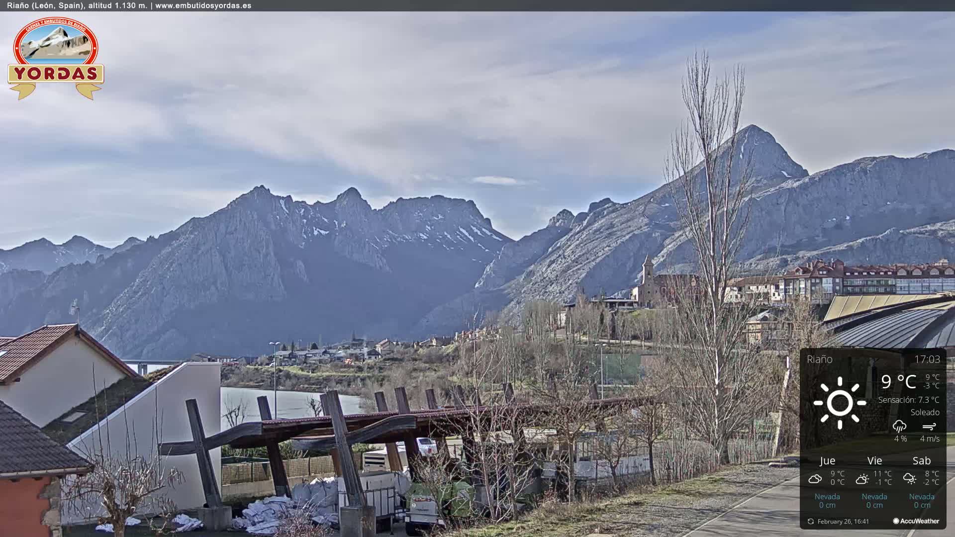 A partly sunny day reveals a town nestled at the base of snow-capped mountains.