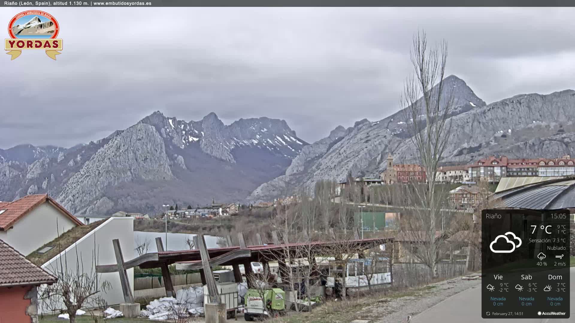 A town nestled at the base of snow-dusted mountains under a cloudy sky.