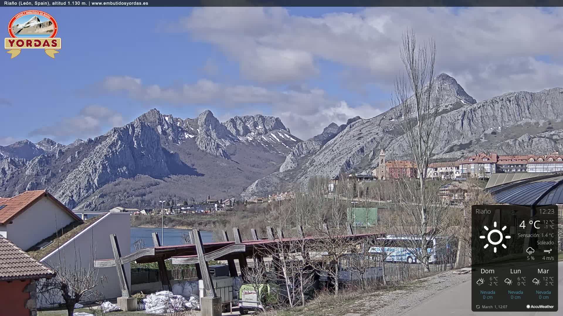 A partly cloudy day reveals a mountain range with some snow, overlooking a town and reservoir.