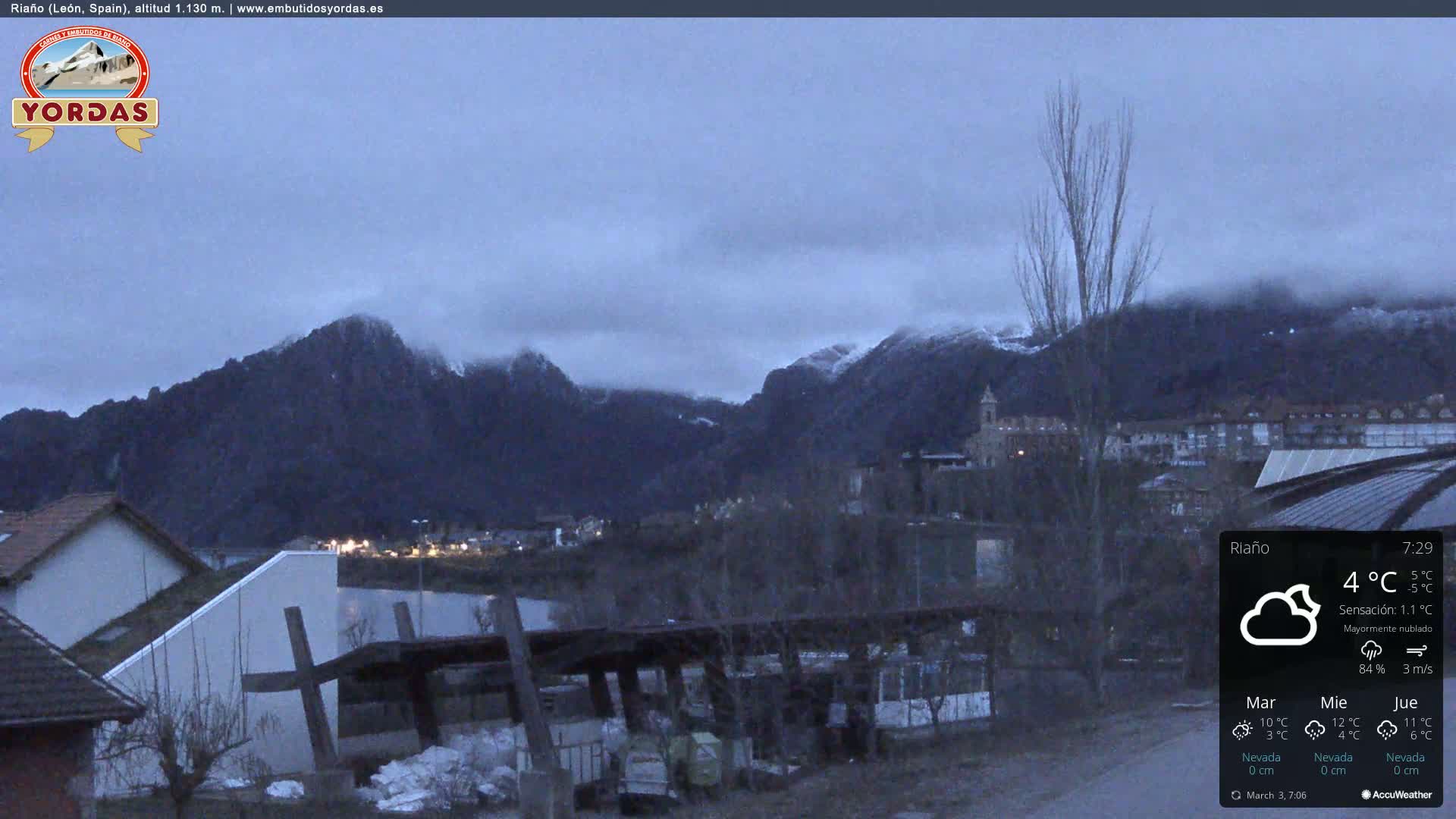 A mostly cloudy, cool evening scene shows a town nestled at the base of snow-dusted mountains.