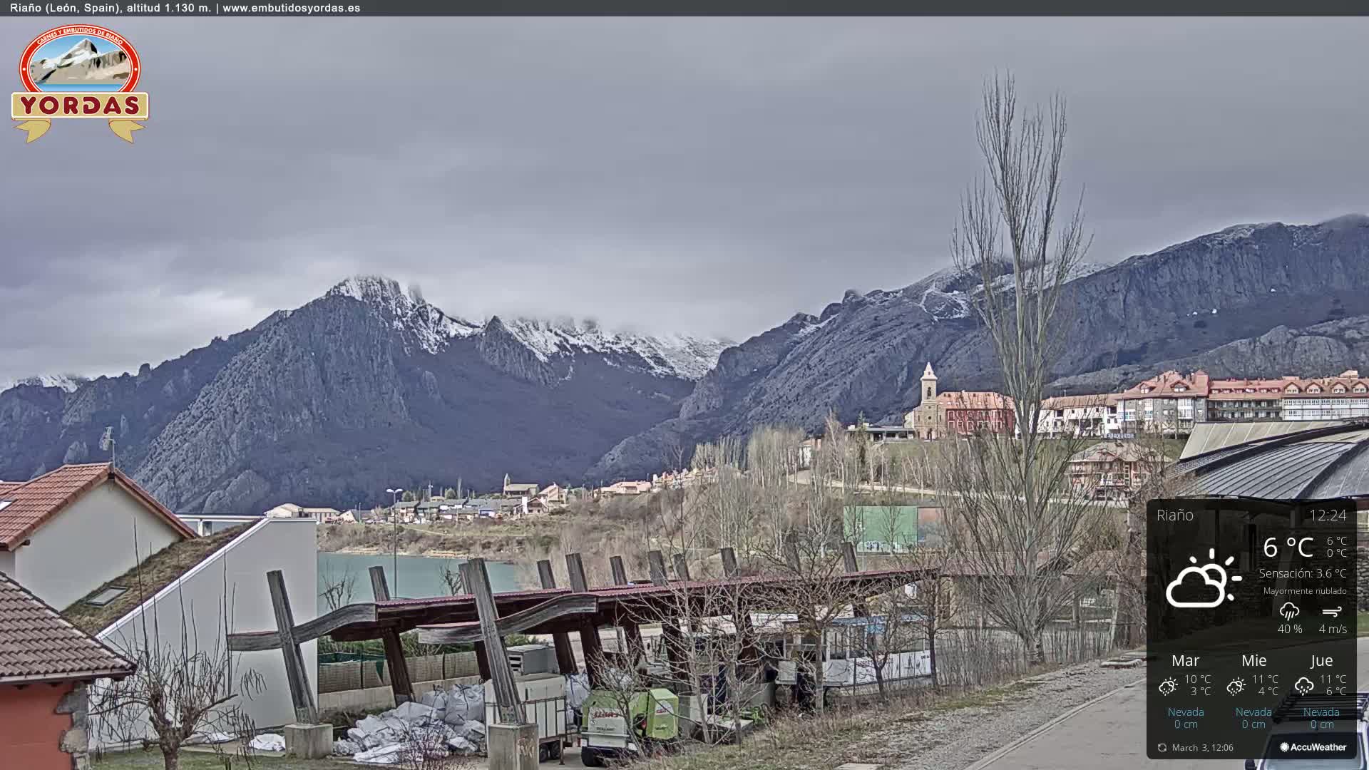 A mostly cloudy day reveals a snow-dusted mountain range overlooking a small town nestled in a valley.