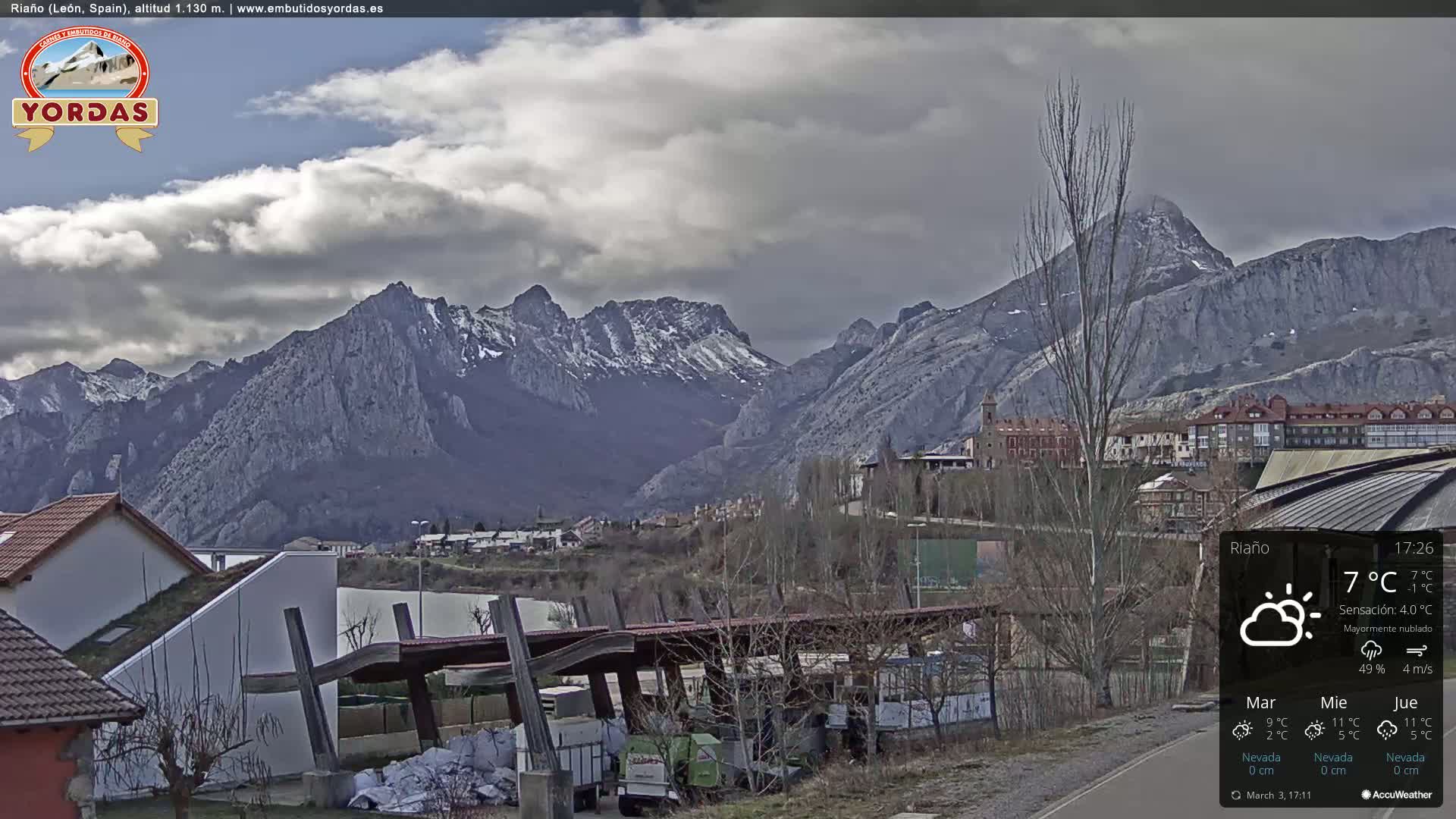 A mostly cloudy view of a town nestled at the base of snow-capped mountains.