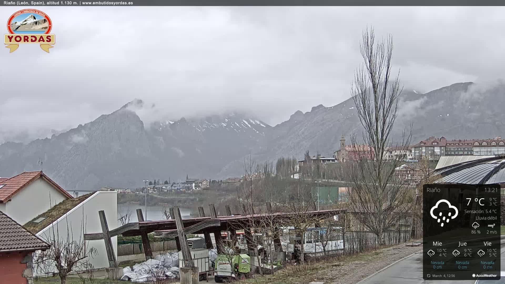 A rain-covered town nestled in a valley, with mountains in the background under a cloudy sky.