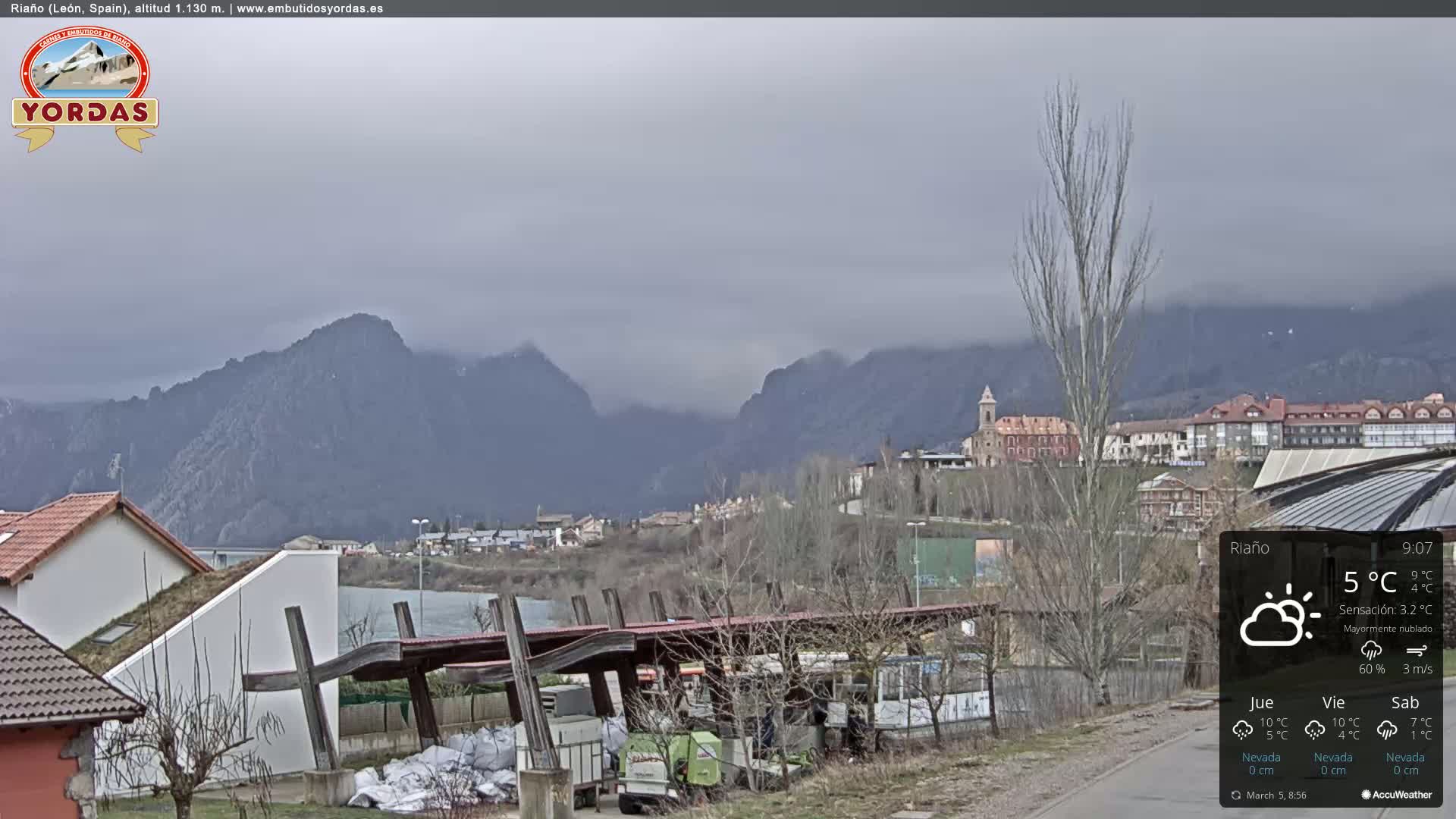 A mostly cloudy view of a town nestled in a valley between mountains.