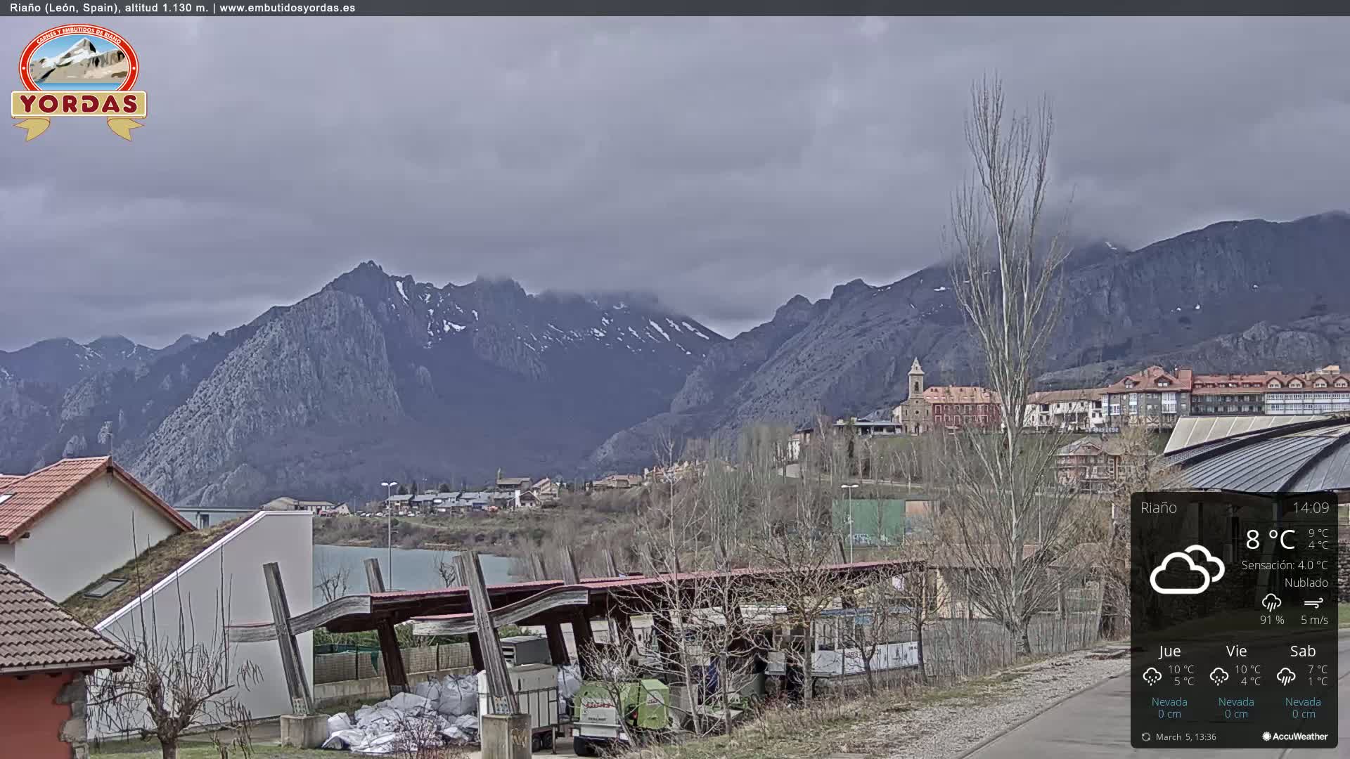 A town nestled in a valley, overlooked by snow-capped mountains under an overcast sky.
