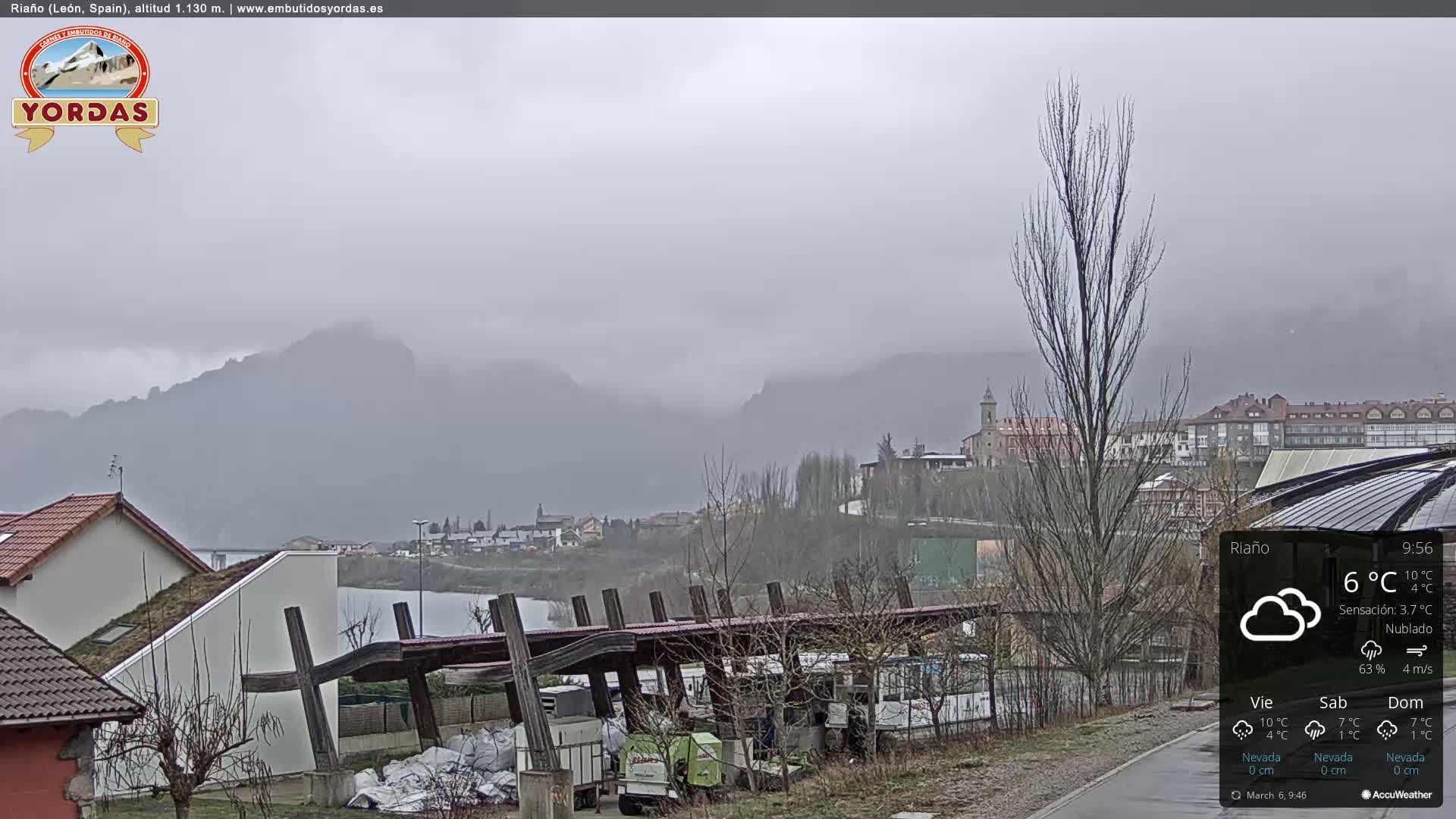A misty, overcast view of a town nestled in a valley between mountains, with buildings and some vegetation visible.